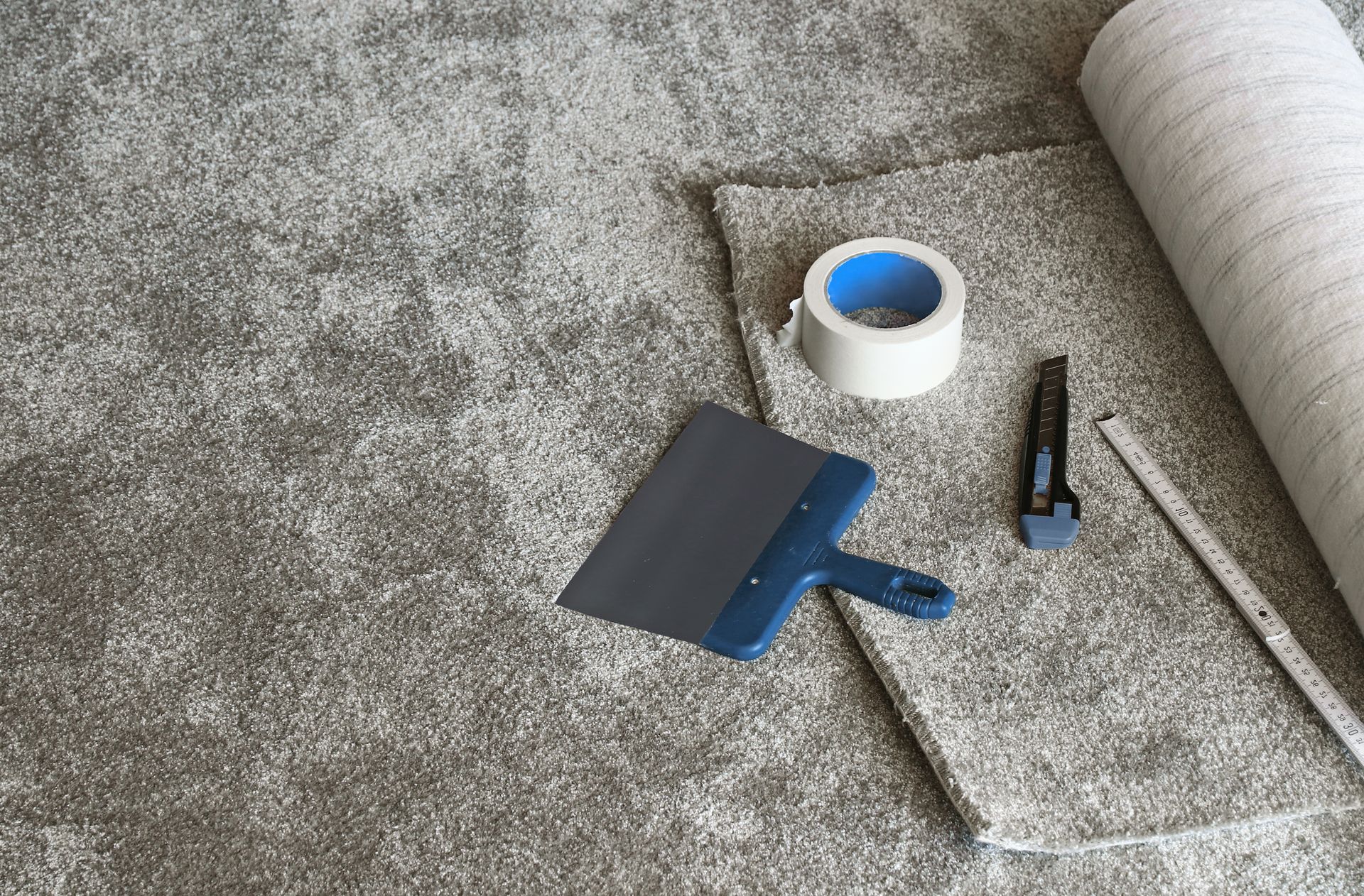 Carpet and tools: tape, knife, putty knife, and roll of carpet for installation.