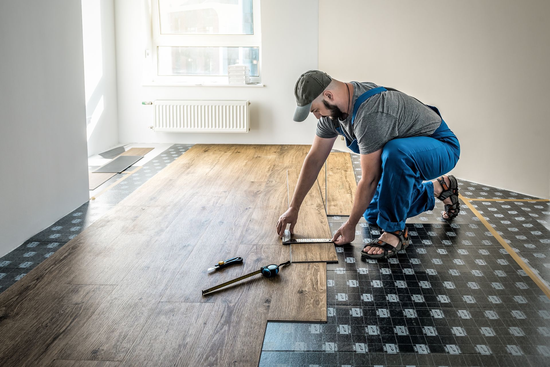 Man installing wood flooring in a room, measuring a plank.
