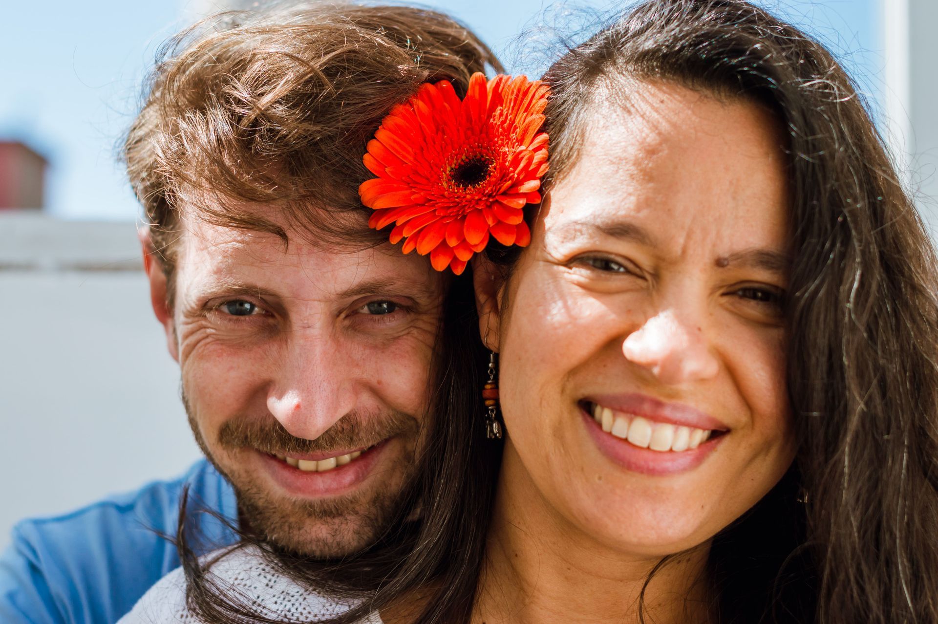 A man and a woman are posing for a picture with a flower in her hair.