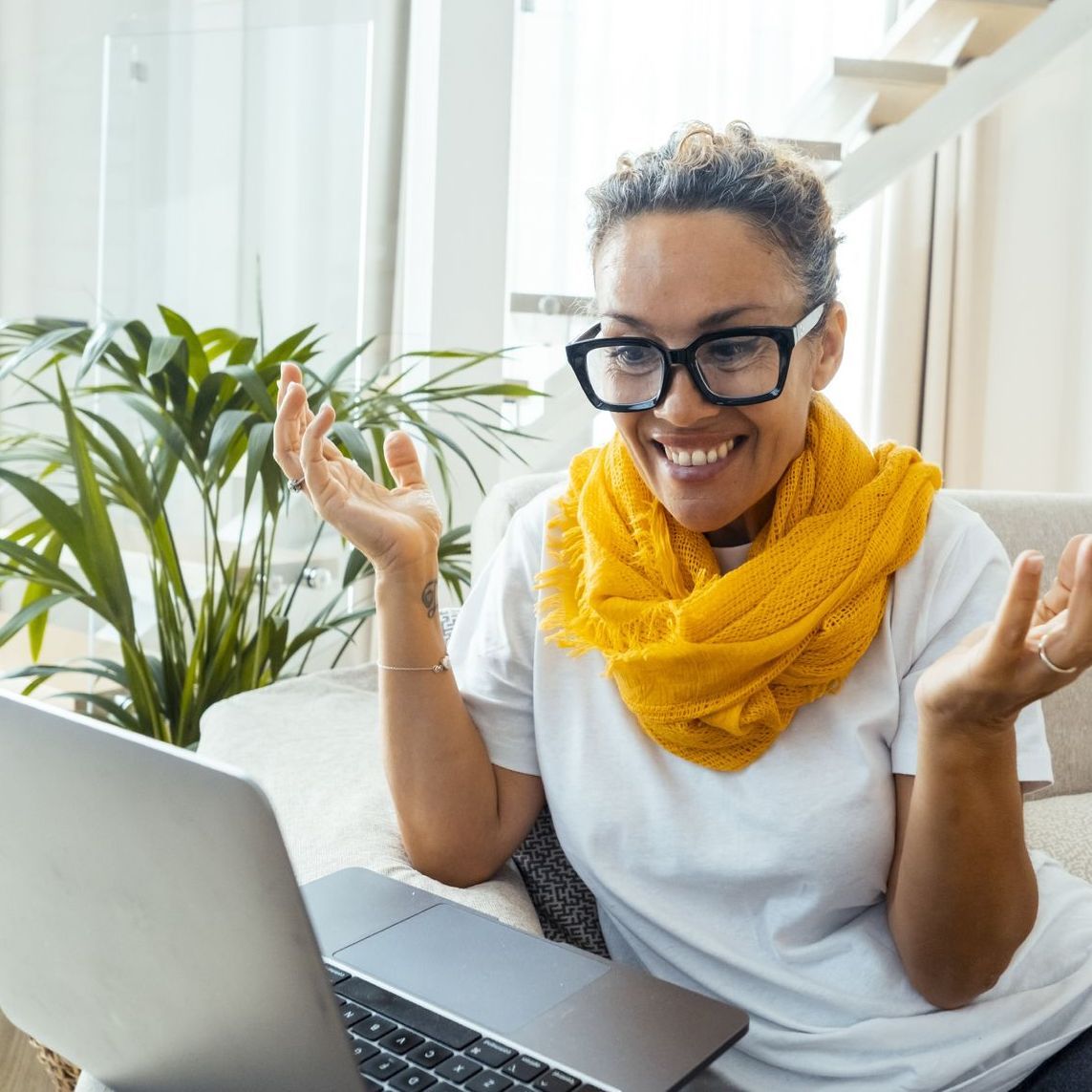 A woman wearing glasses and a yellow scarf is sitting in front of a laptop computer.