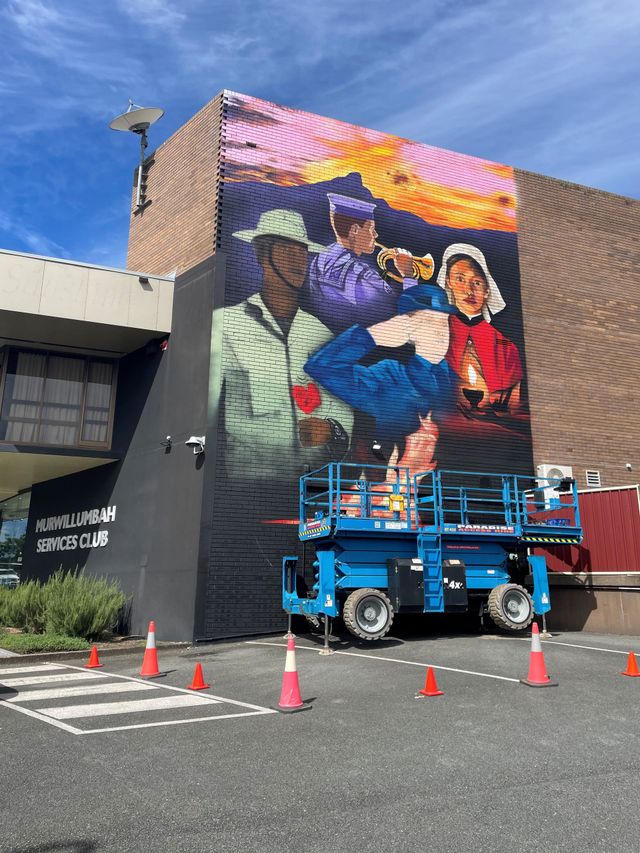 Mural painted on a building beside a blue lift truck, with orange cones in a parking lot.