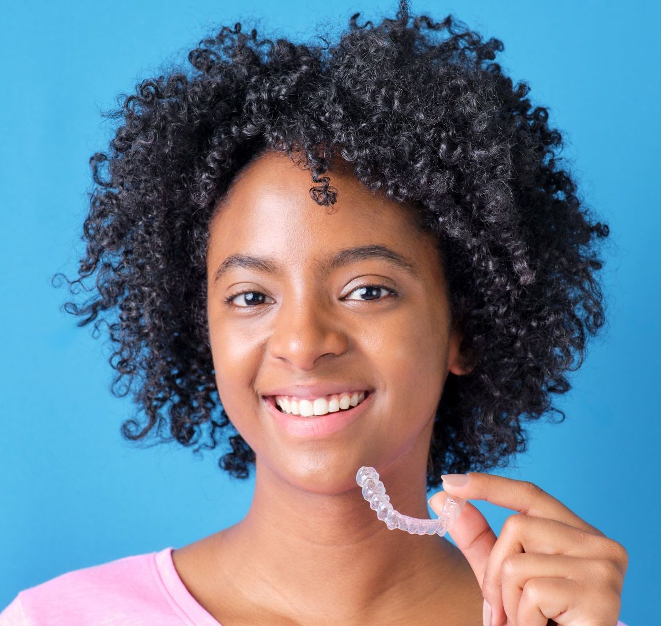 A young woman with curly hair is holding a clear brace on her teeth.