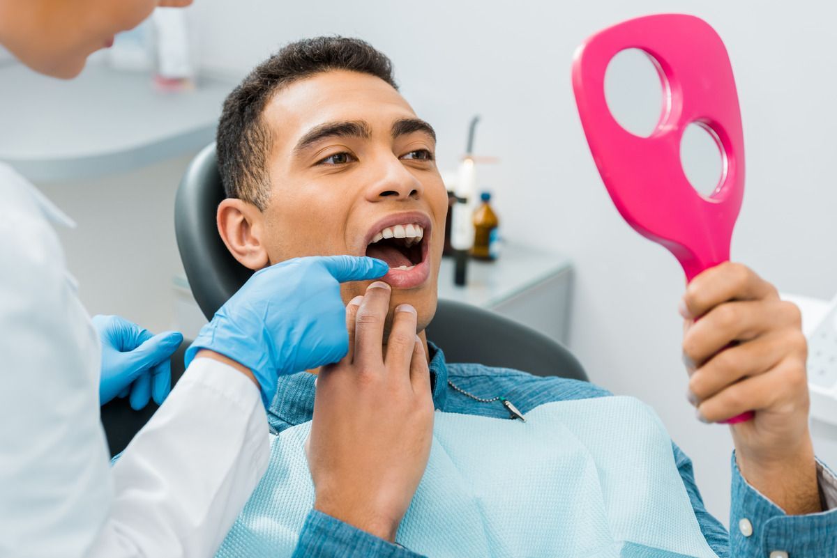 A man is sitting in a dental chair looking at his teeth in a mirror.
