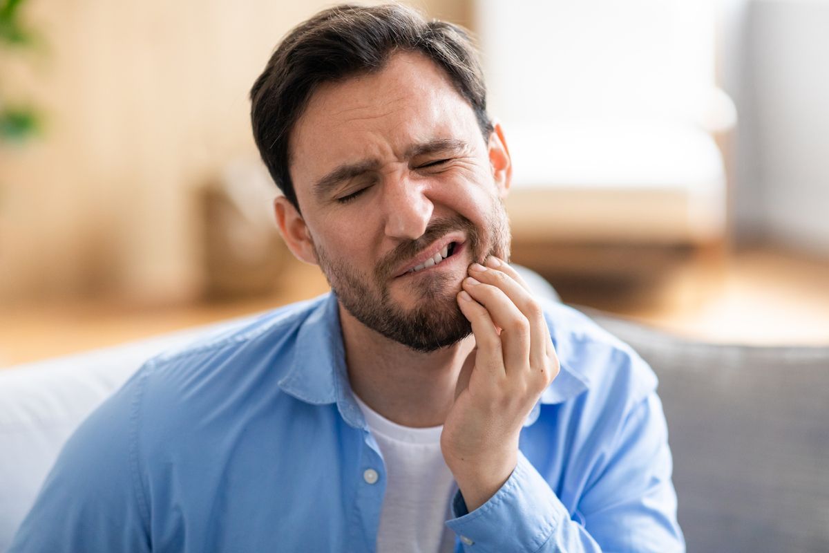 Man grimacing and holding his jaw, suggesting tooth pain, in a bright indoor room