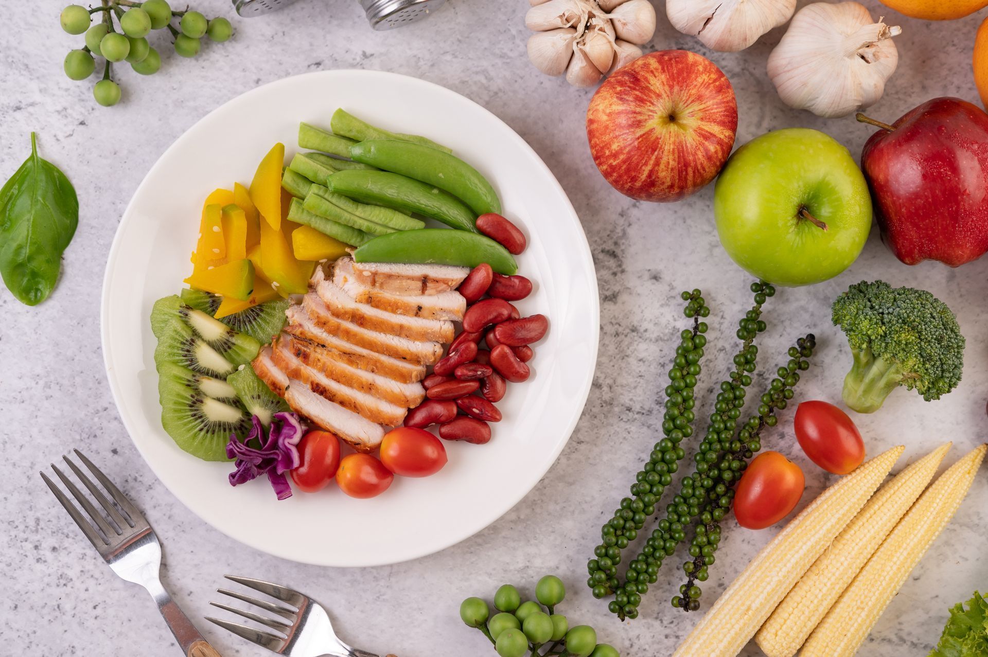 A plate of grilled chicken with green beans, red beans, kiwi, peppers, and fresh produce