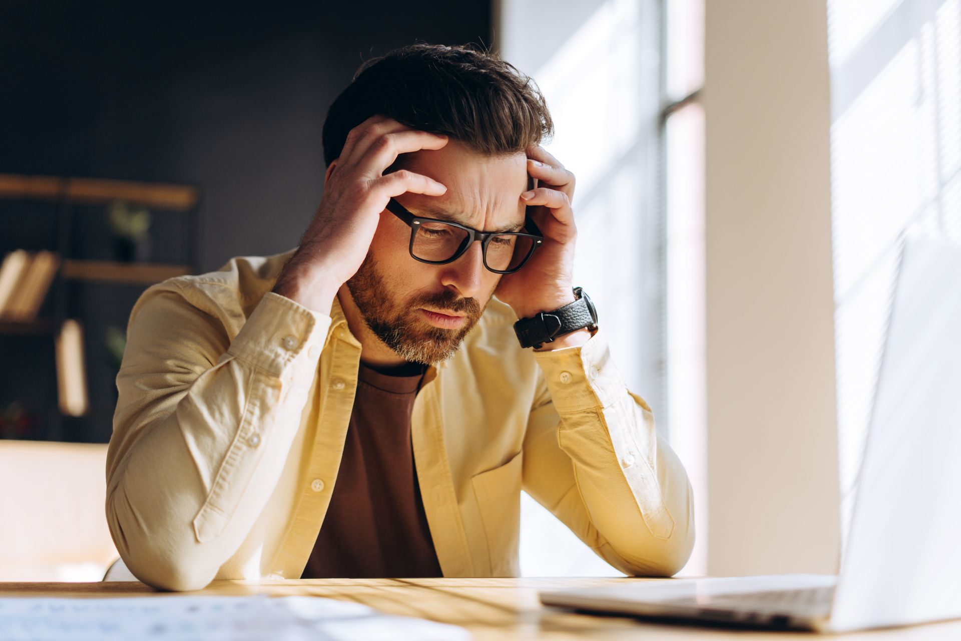 Man sitting at a desk with his hands on his head showing stress and anxiousness