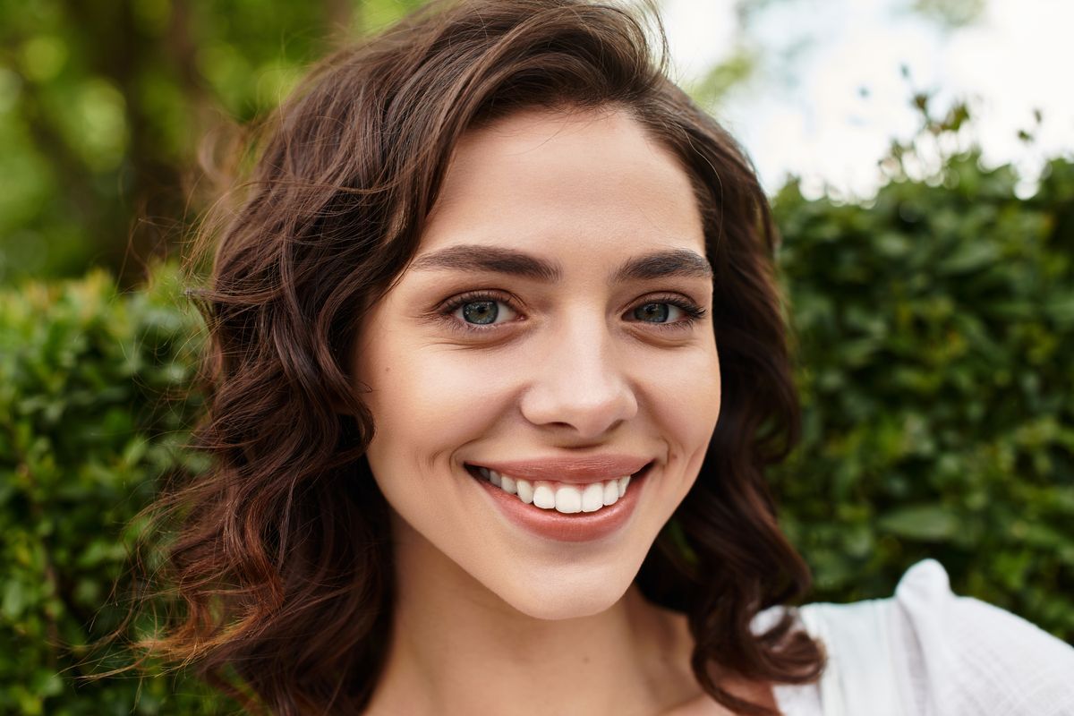 Smiling woman with curly brown hair outdoors in front of green foliage