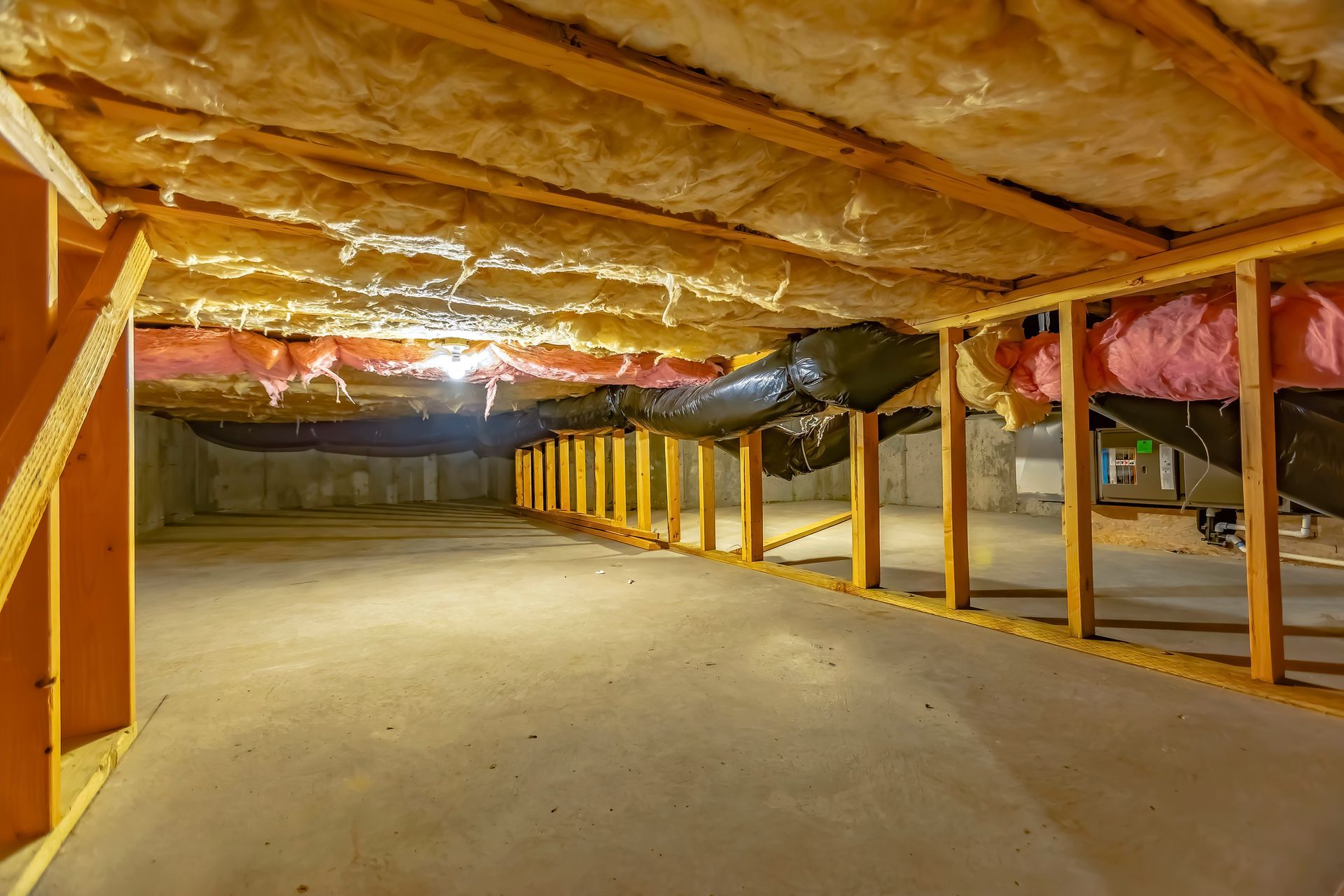 A basement under construction with insulation and pipes.