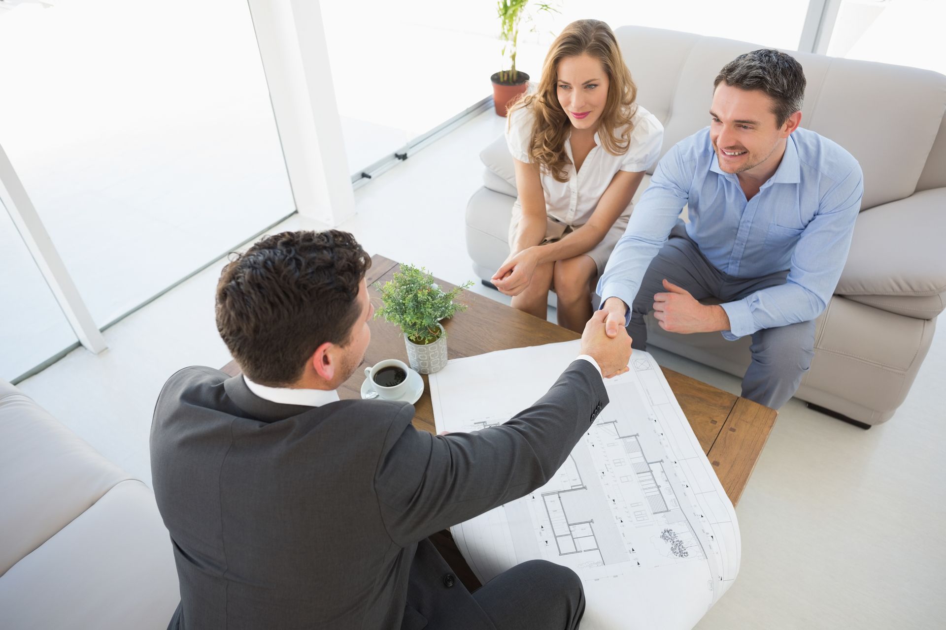 A man is shaking hands with a couple while sitting on a couch.