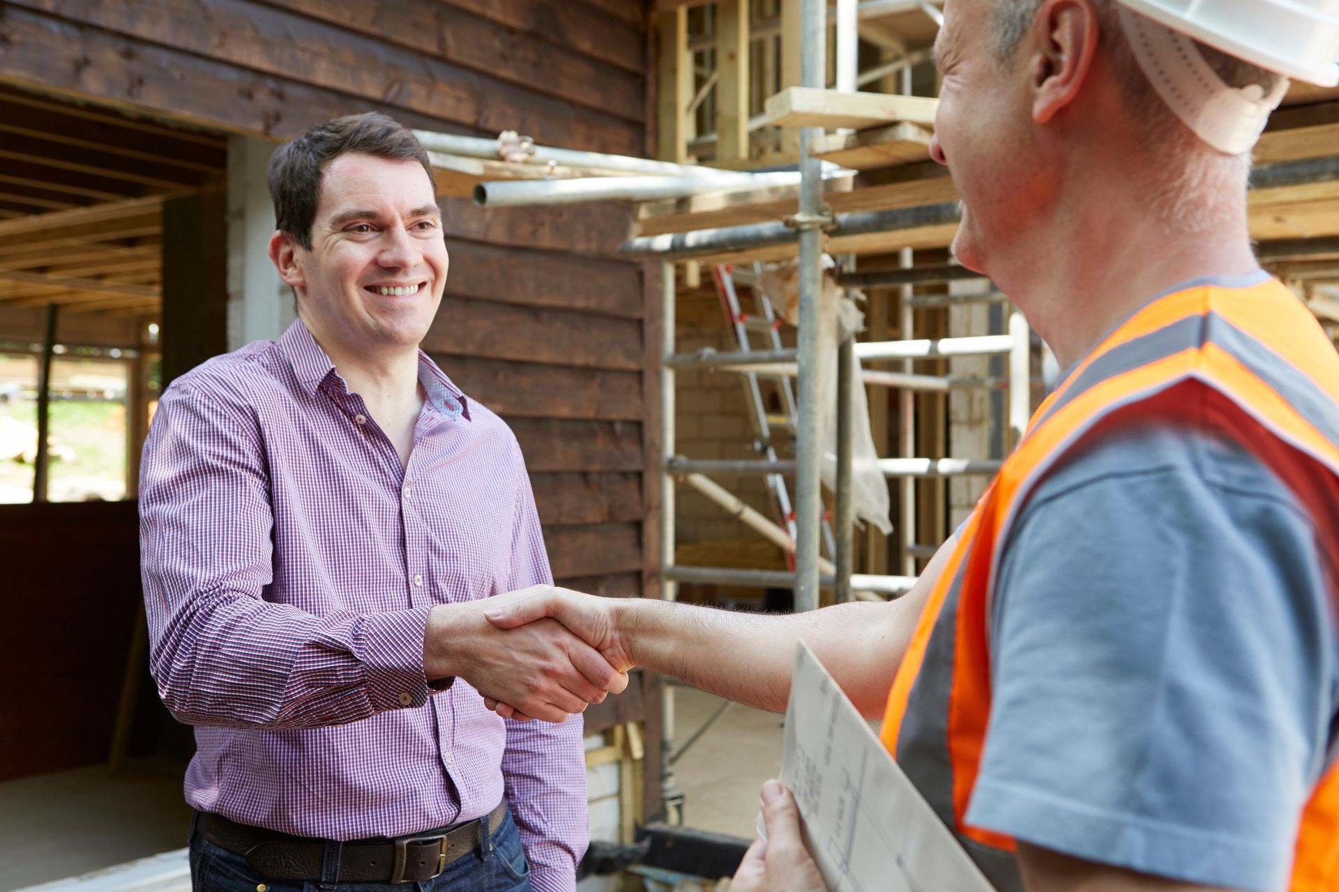 Two men shaking hands in front of a building under construction