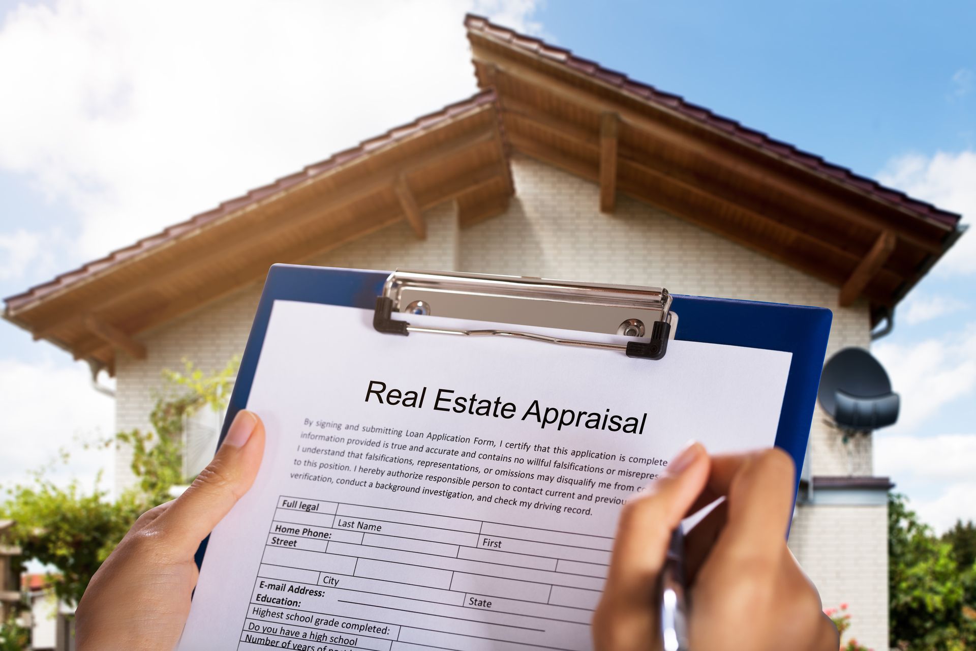 A person is holding a clipboard with a real estate appraisal on it in front of a house