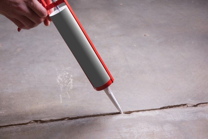 Hand using a caulking gun to apply sealant to a crack in a concrete floor.