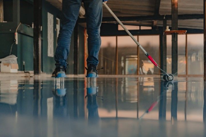 Person in jeans rolling blue epoxy floor with a tool in an open-air building.