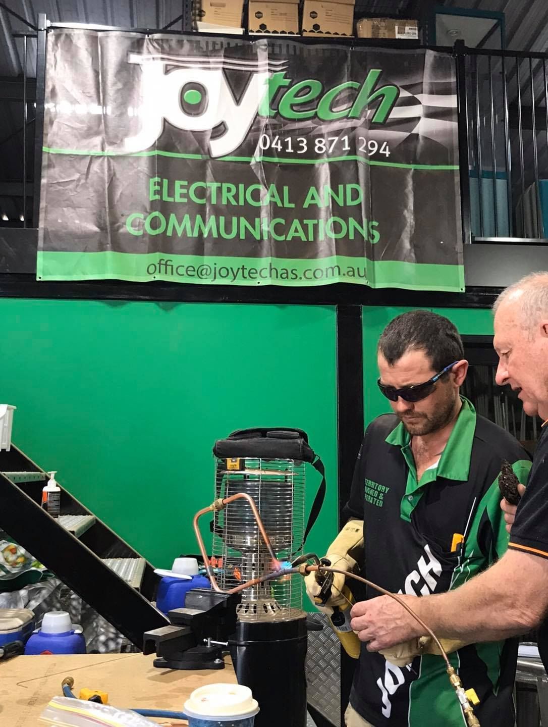 Two Men Are Working On A Machine Under A Joytech Banner — Joytech In Ciccone, NT