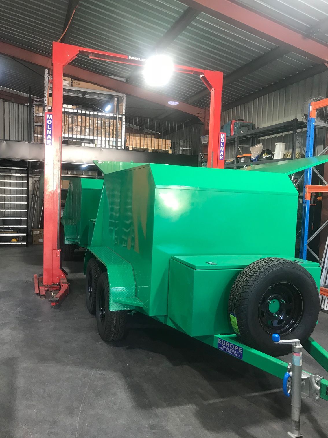 A Green Trailer Is Parked In A Garage Next To A Red Crane — Joytech In Ciccone, NT