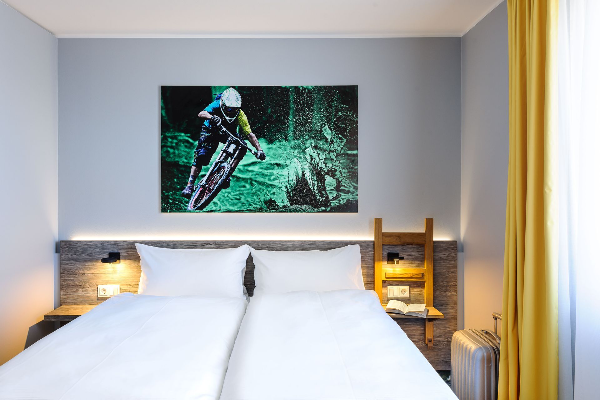 Modernes Schlafzimmer mit ordentlich gemachtem Bett, Holzkopfteil mit Beleuchtung und Fahrradmotiv als Wandbild über dem Bett