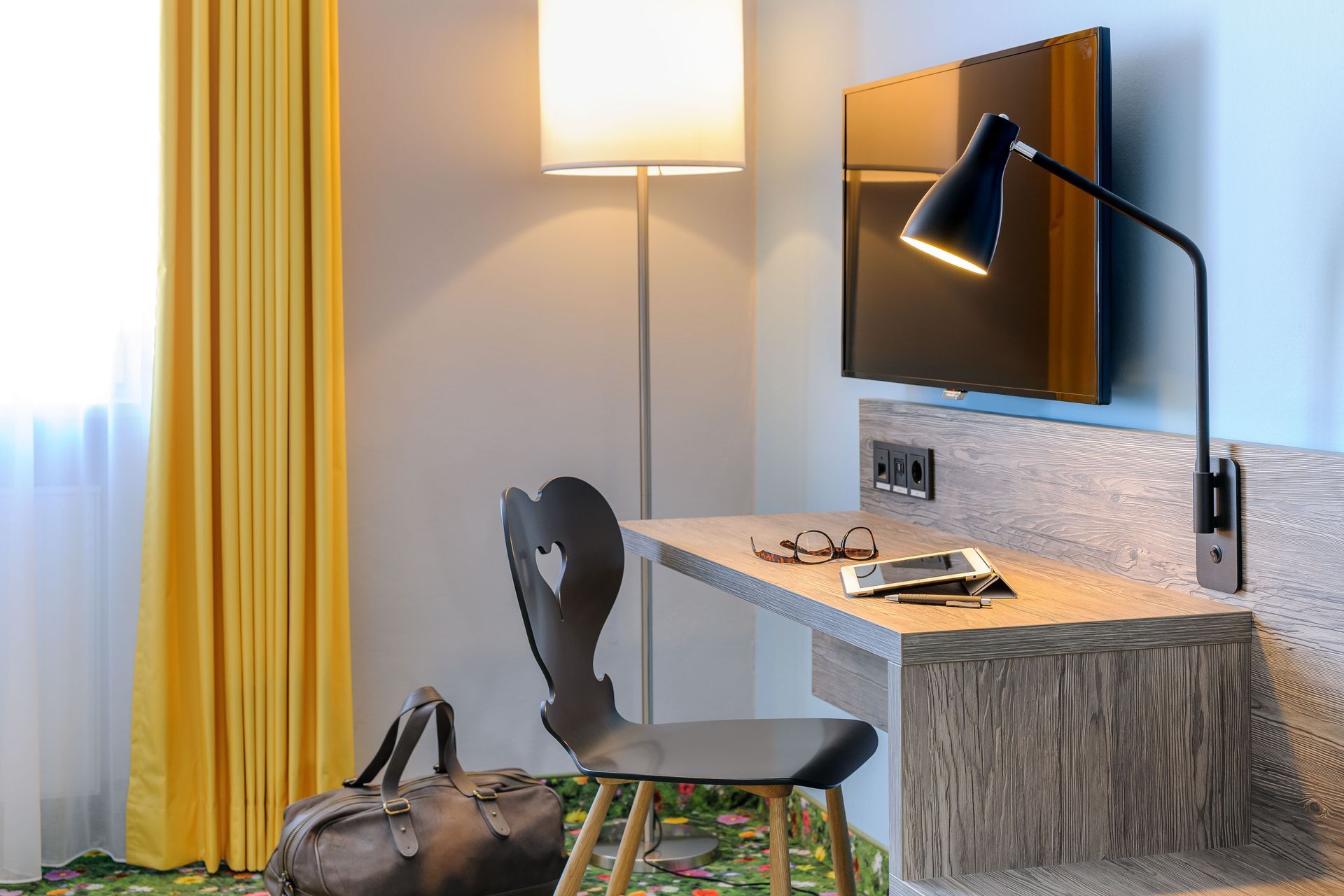 Moderne Wohnzimmerecke mit Schreibtisch, Stuhl, Lampe, Wandspiegel und Tasche vor dem bodenlangen Vorhang