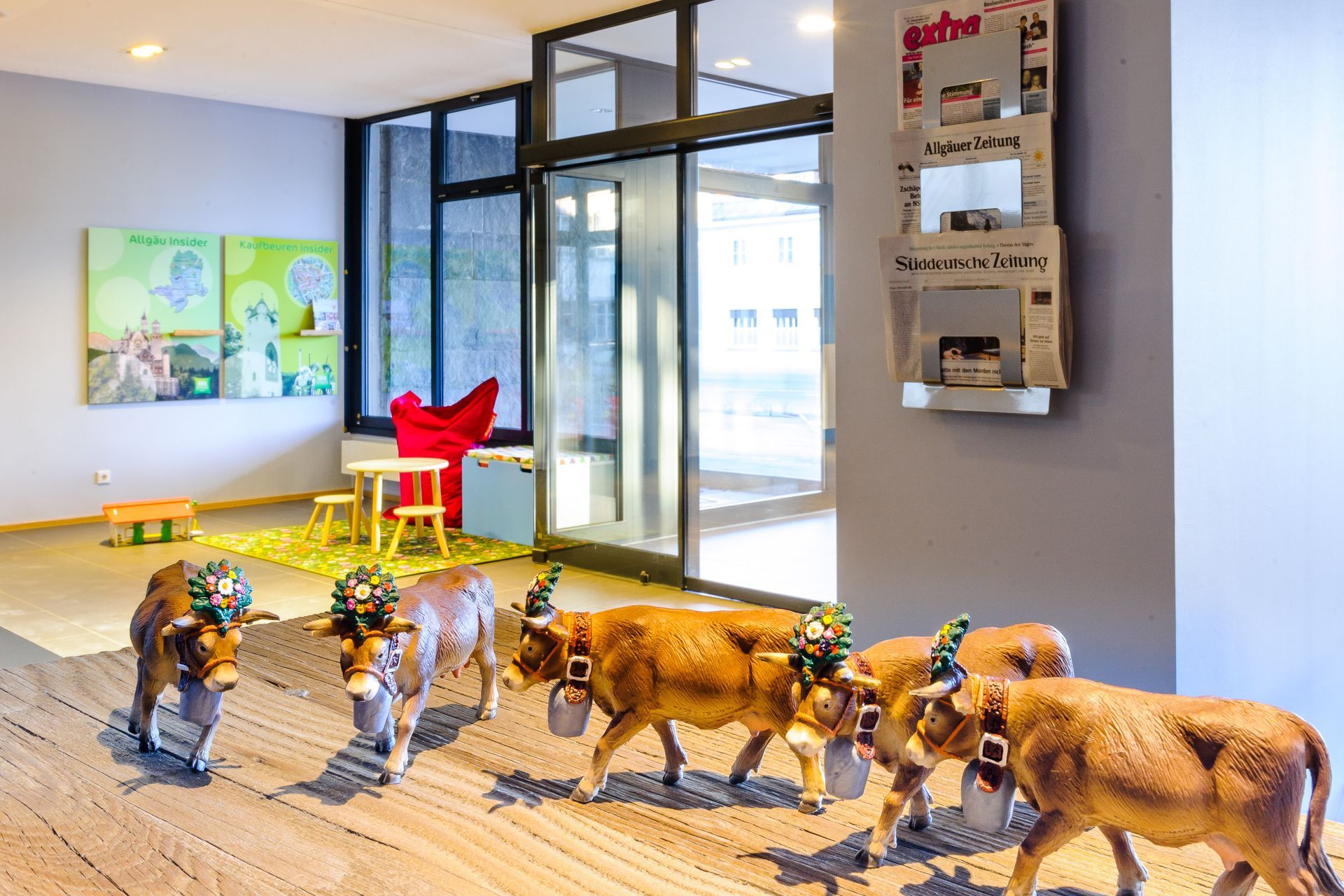 Spielzeugtiere und kleine Figuren auf einem Teppich in einem hellen, modernen Zimmer mit Glastüren und Wandbildern