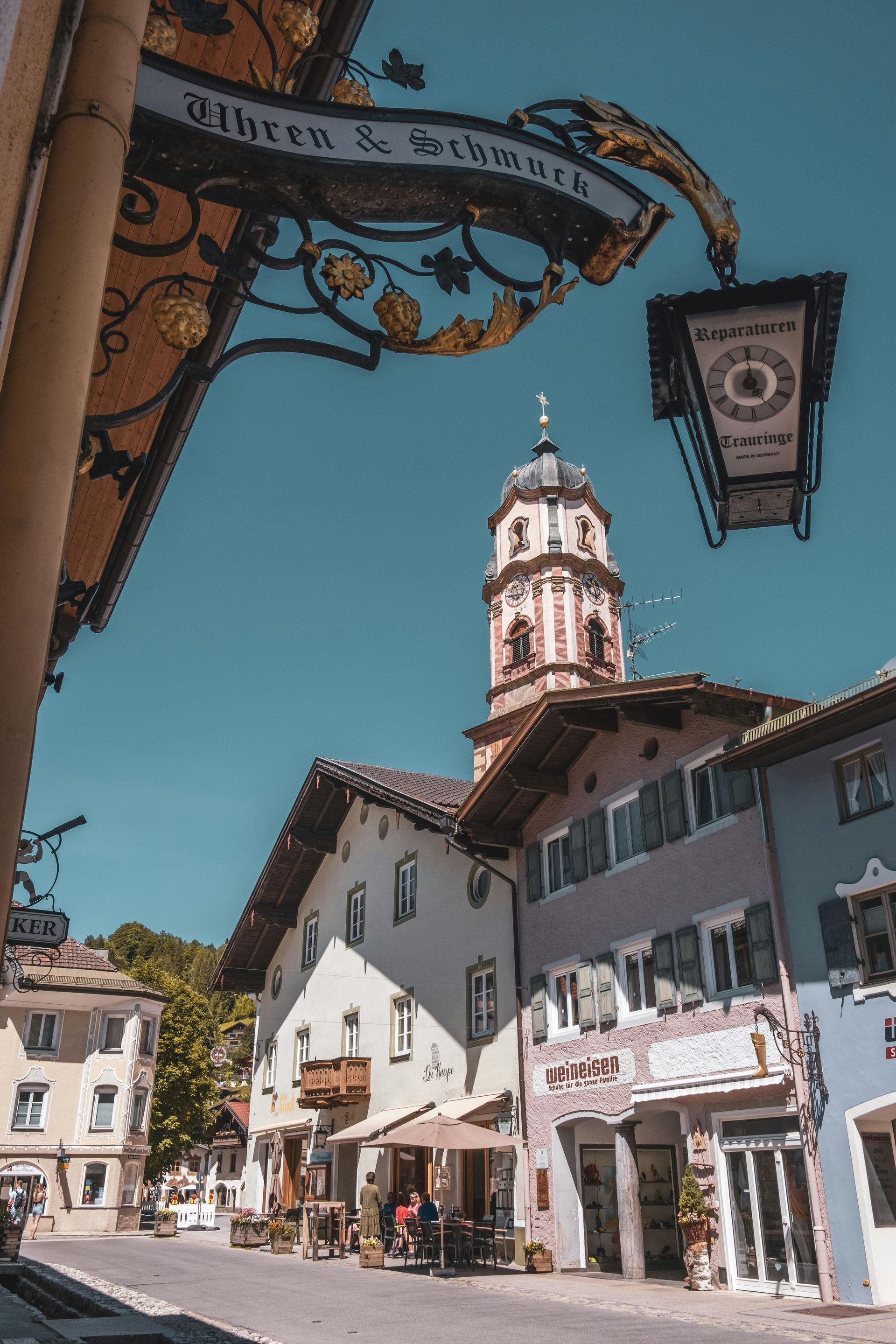 Sonnenbeschienene europäische Straße mit weißen Gebäuden und einem Uhrturm unter strahlend blauem Himmel