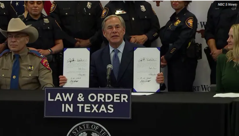 Man at podium reading papers at a Texas law and order event, police officers standing behind him
