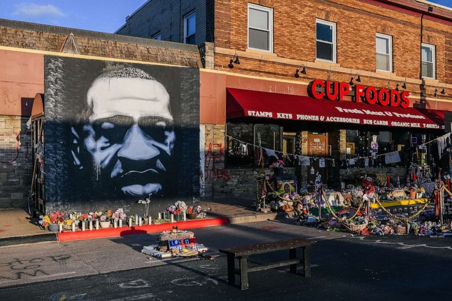 Mural of George Floyd beside the CUE Foods storefront with flowers and candles on the sidewalk