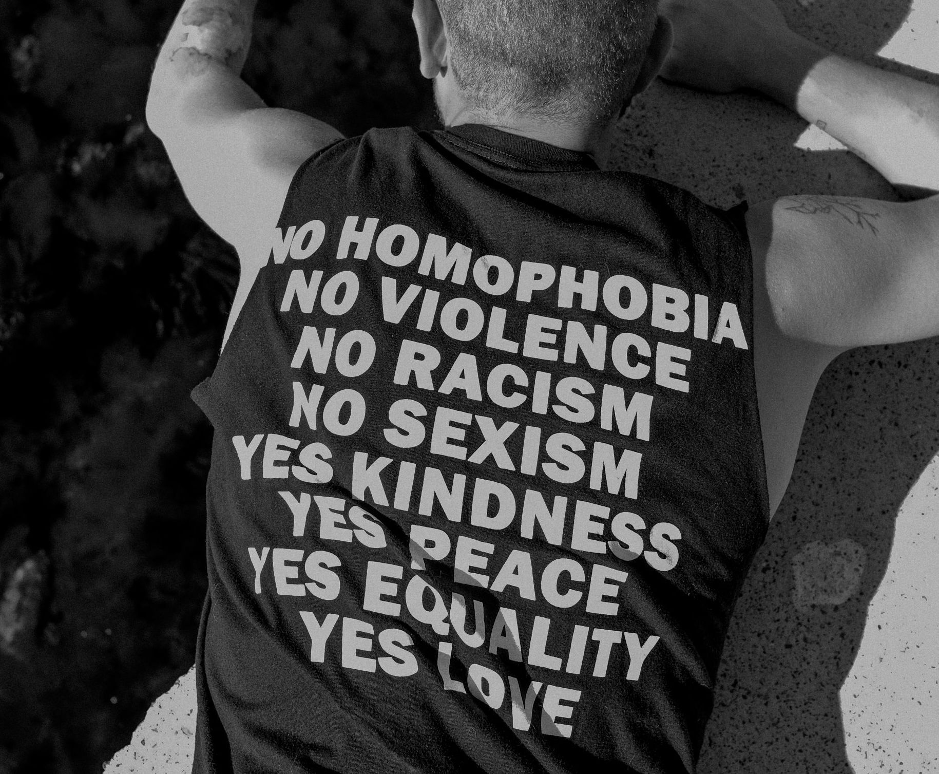 Person wearing a black shirt with anti-hate slogans: no homophobia, violence, racism, sexism; yes kindness, peace, equality, love
