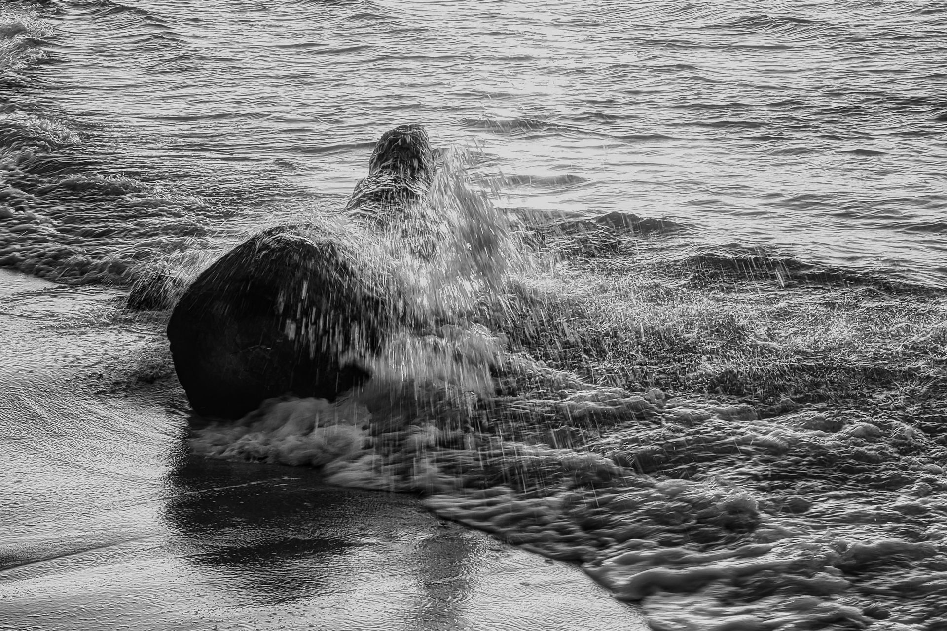 Person splashing in shallow surf beside a large dark ball on a rocky beach