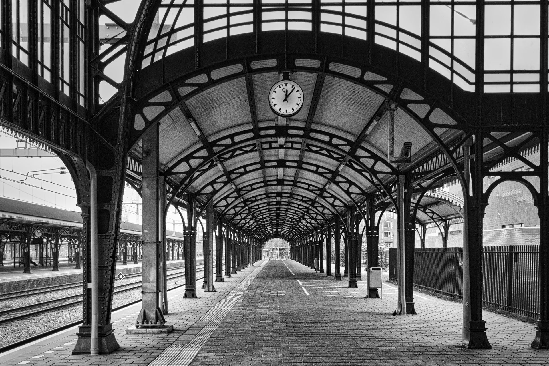 Empty railway platform with arched glass roof and central clock in black and white