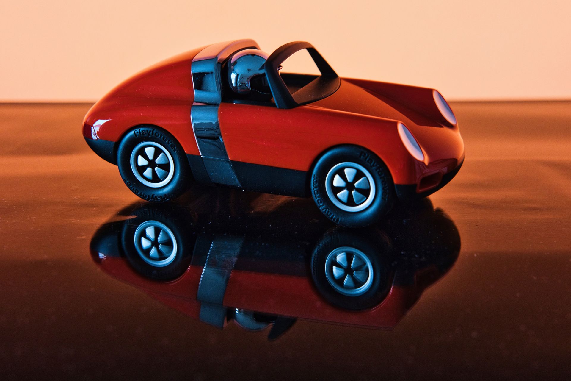 Orange toy car on a glossy black surface, reflected beneath it, against an orange background