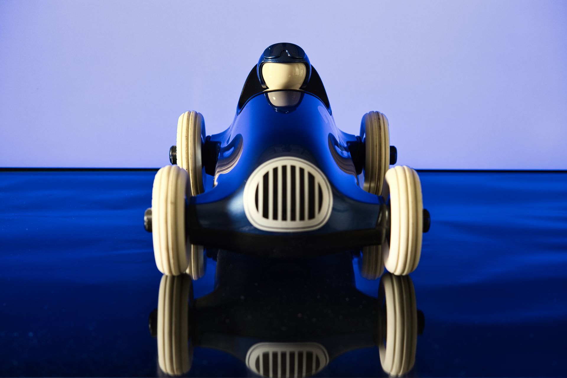 Blue toy race car viewed from the front on a reflective surface, with a driver figure visible in the cockpit