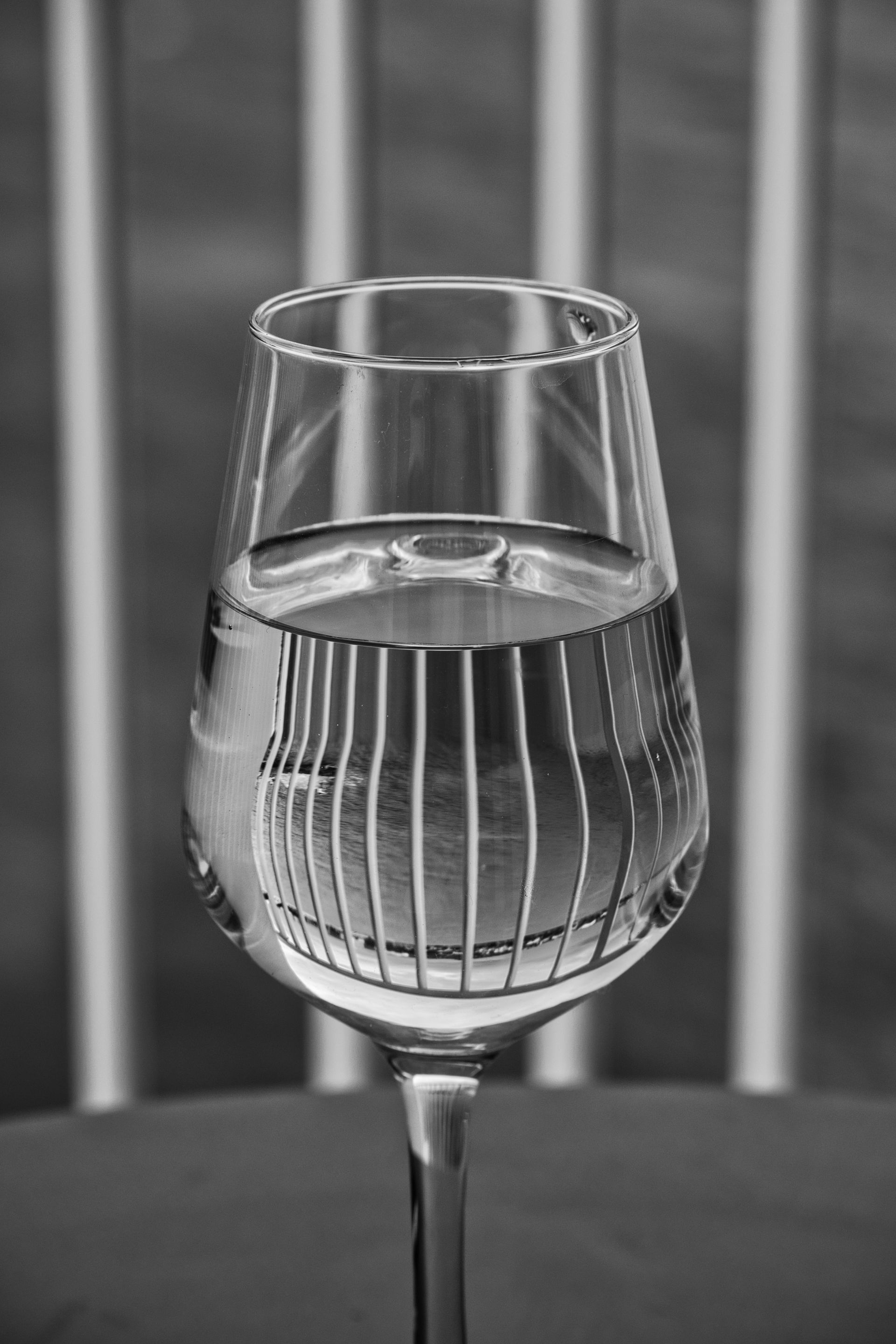 A wine glass filled with water on a table, with vertical reflections in the liquid.