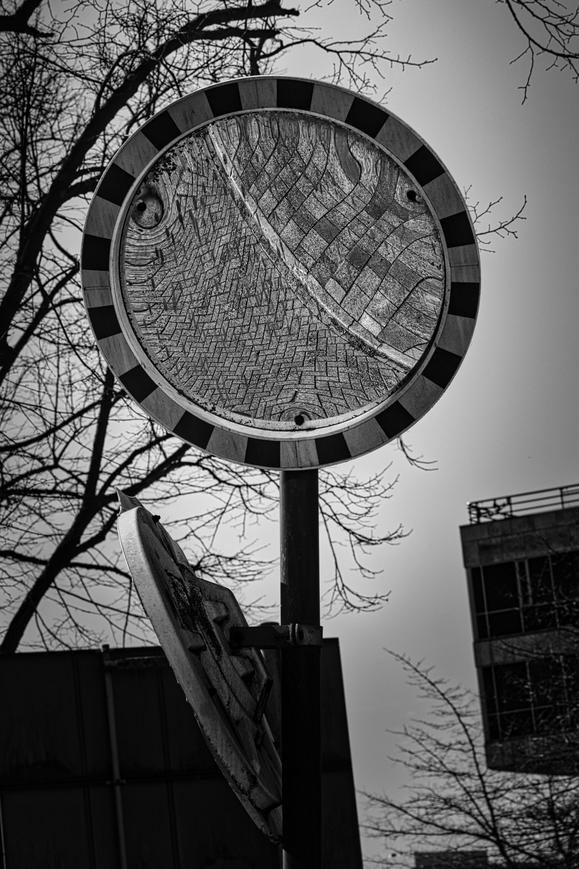 Round street sign amid bare trees and buildings in black-and-white.