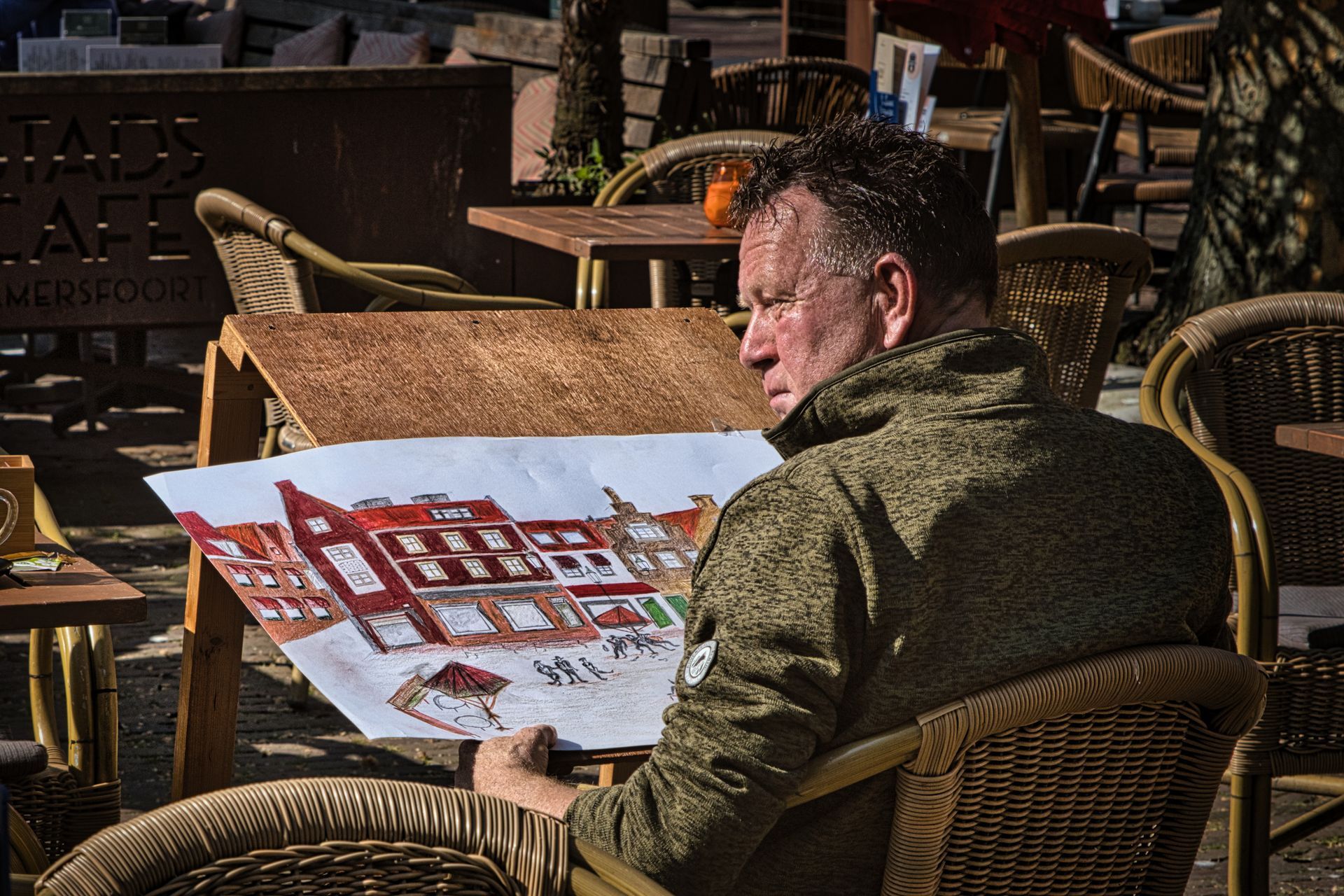 Artist painting a red building sketch at an outdoor café table