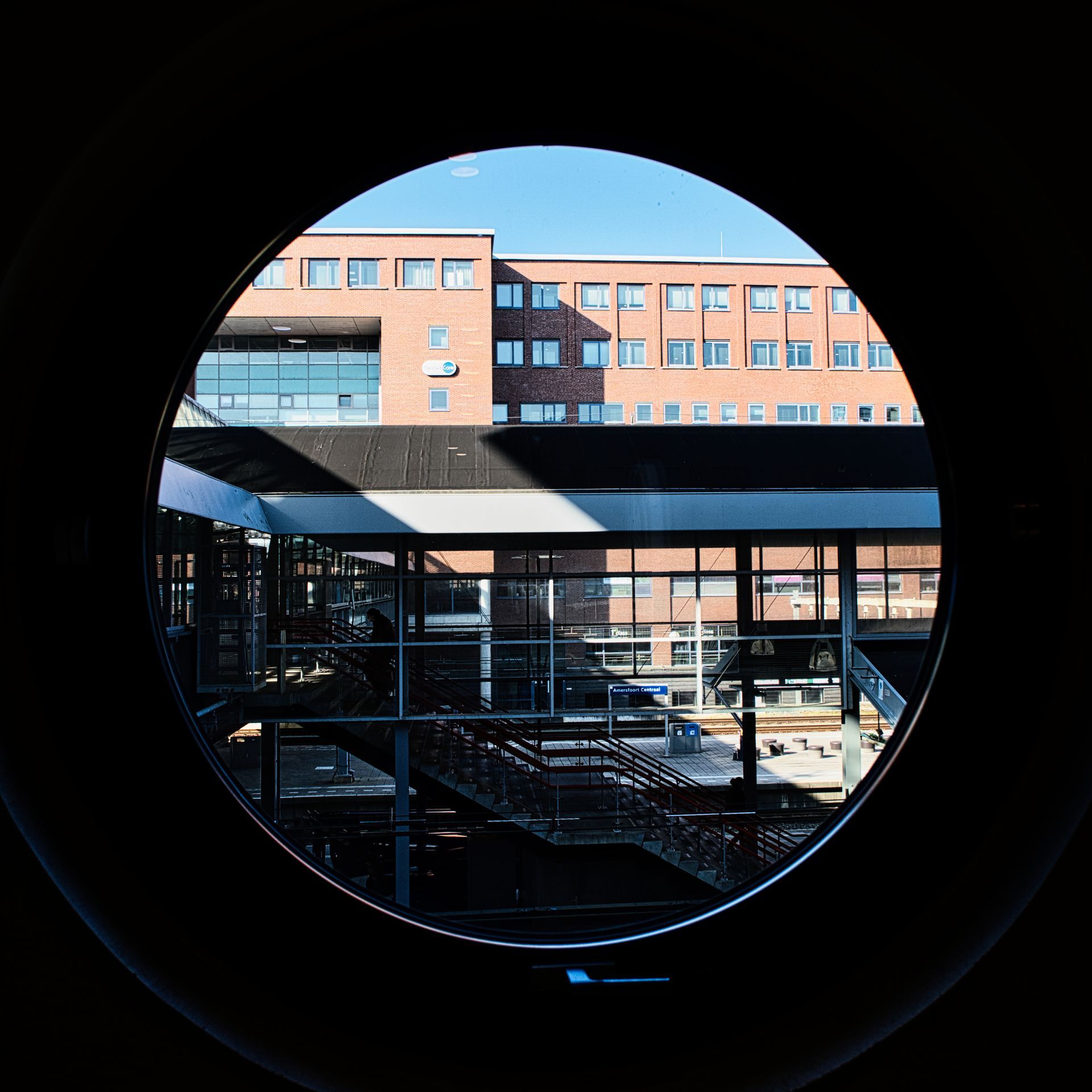 Circular view of a brick office building courtyard through a dark opening, with blue sky above.