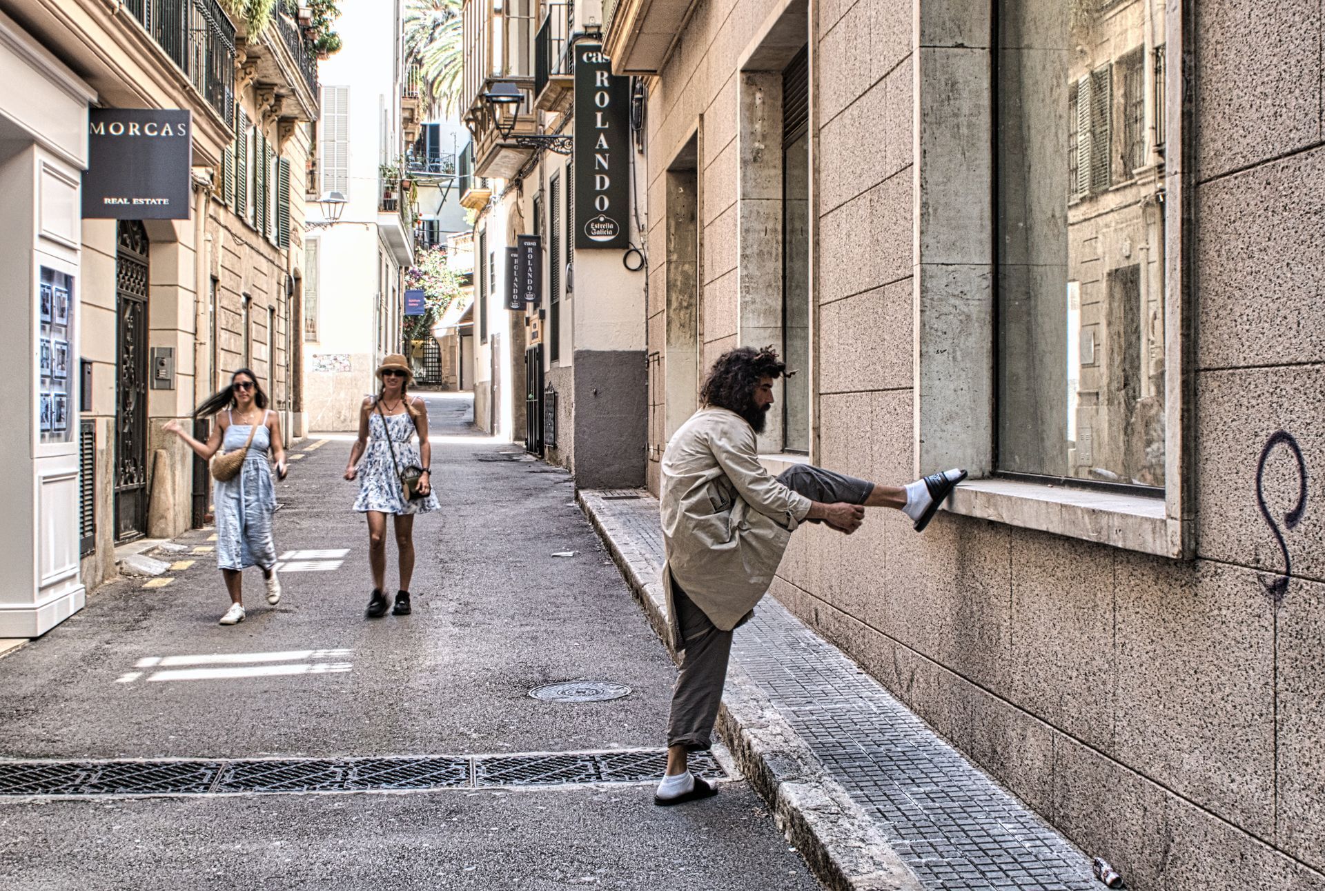 Man is lifting his leg while two people are walking down a narrow stone alley 