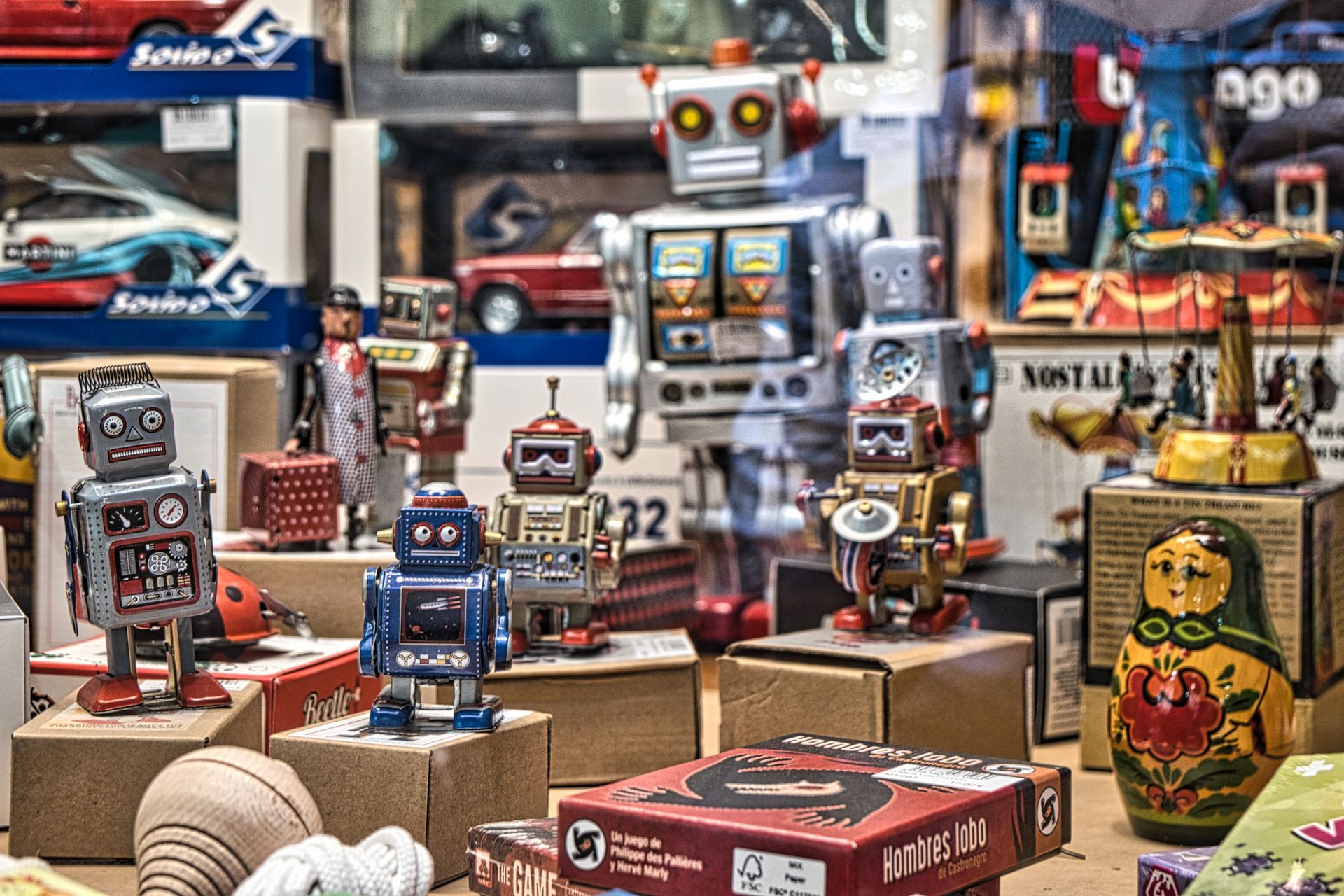 Small toy robots displayed on cardboard boxes in a shop window, with colorful packaging behind them