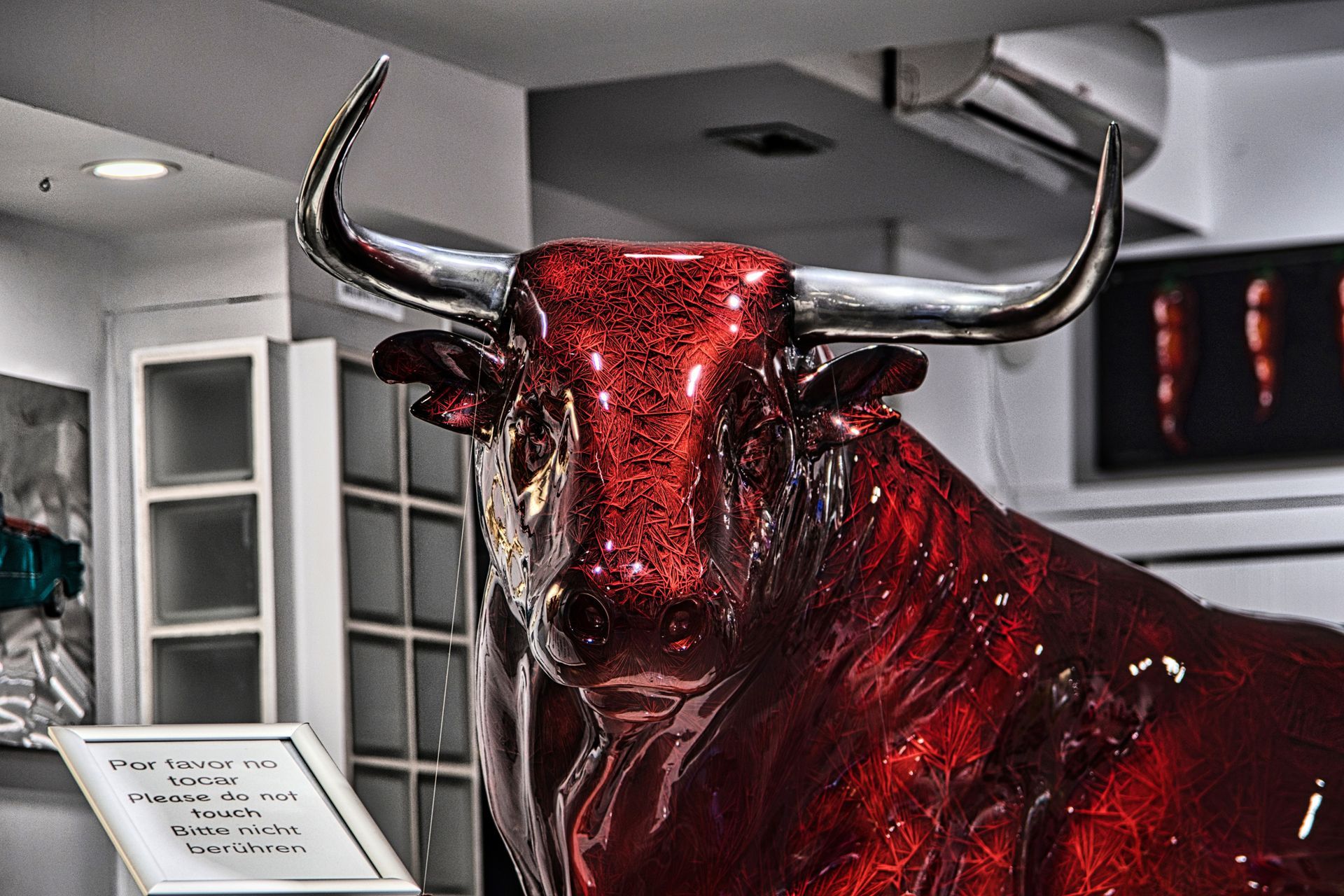 Red glittering bull statue with long horns displayed in a modern indoor room.