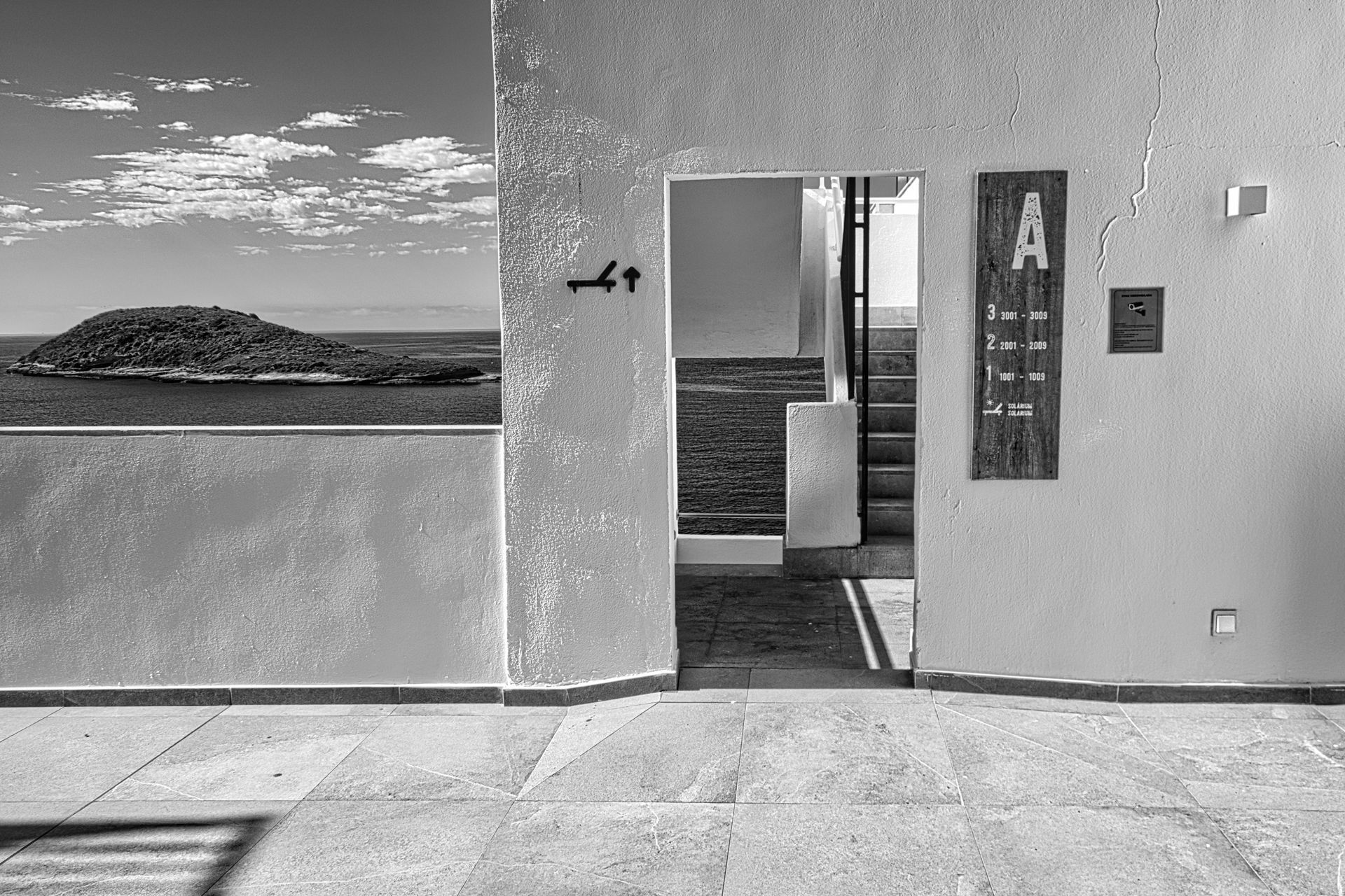 Concrete courtyard with ocean view, open doorway, and wall-mounted art in black and white.