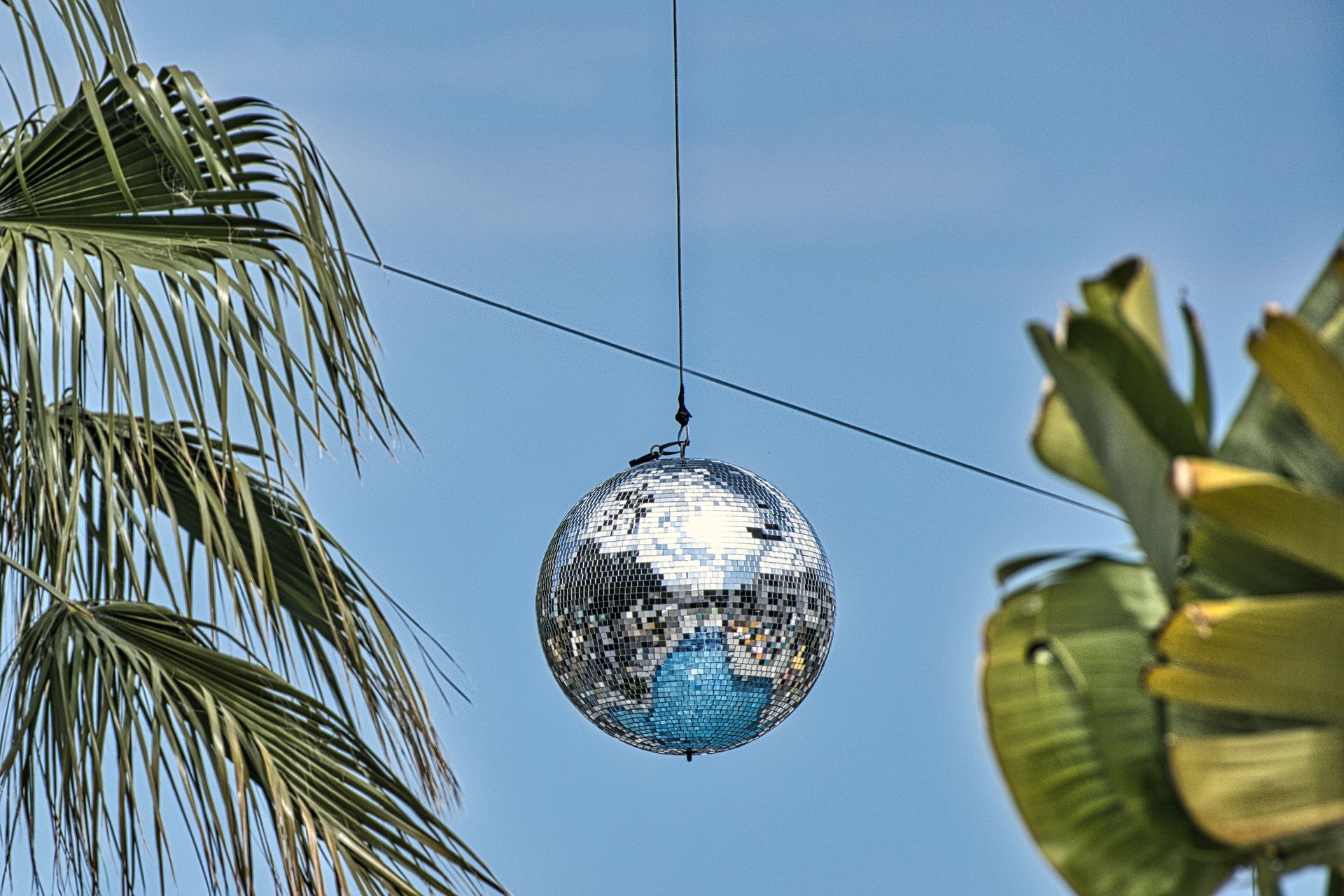 Disco ball hanging on a wire between palm leaves against a blue sky