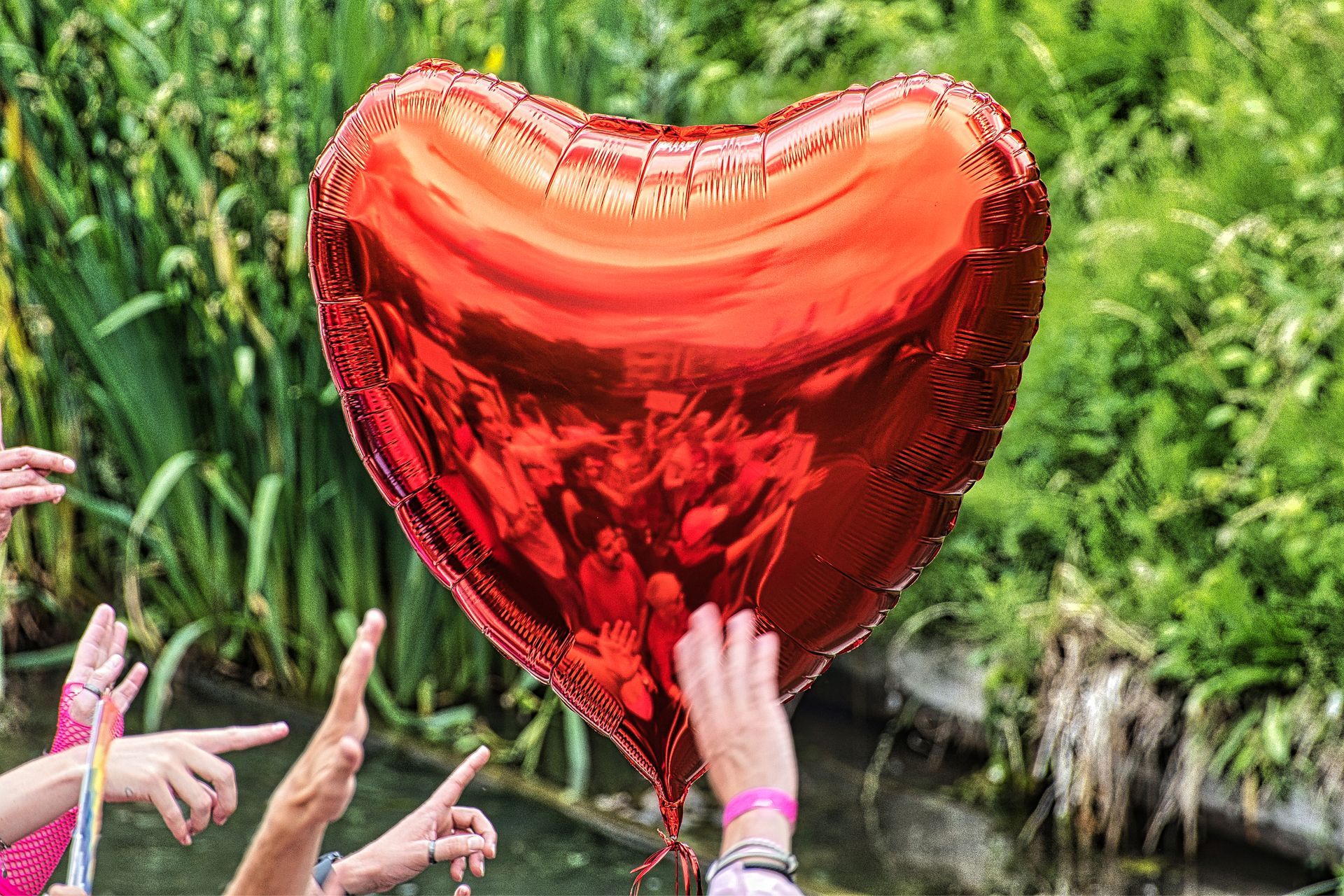Red heart-shaped balloon held by hands outdoors with greenery in the background