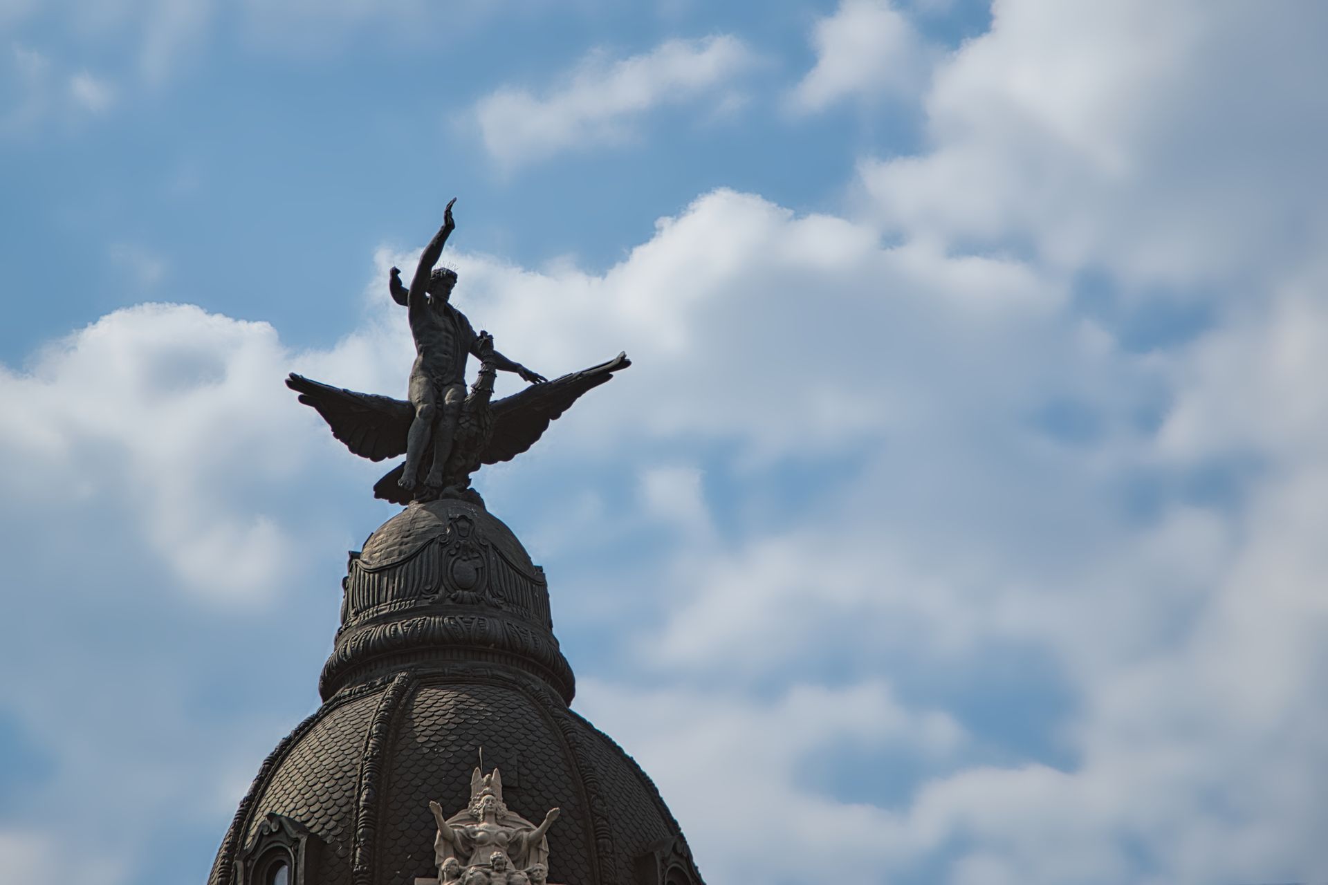 Winged statue atop a domed building against a cloudy blue sky