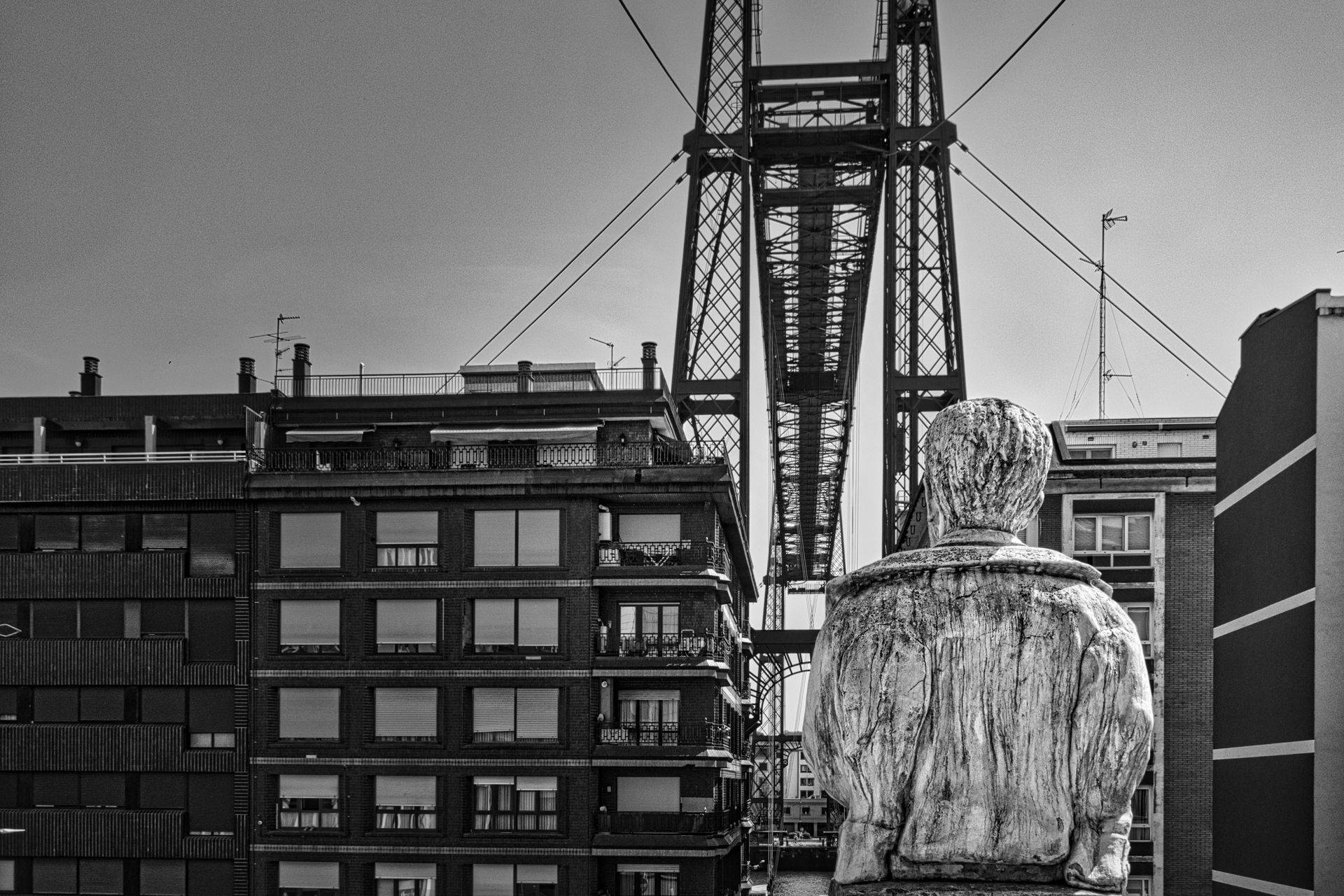 Black-and-white cityscape with a crane, apartment buildings, and a large wrapped object in the foreground