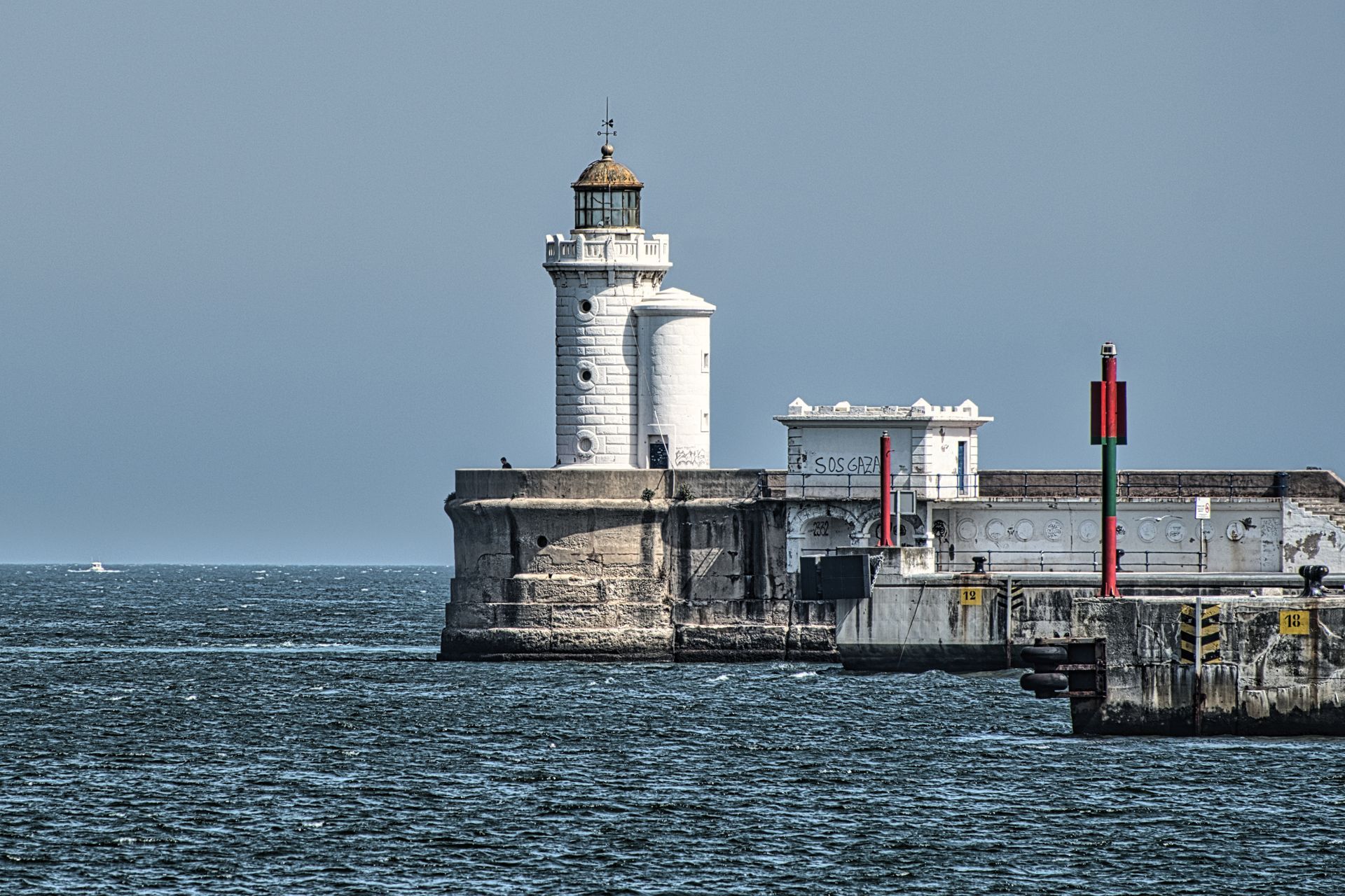 White lighthouse on a stone pier beside choppy blue-gray water under a clear sky