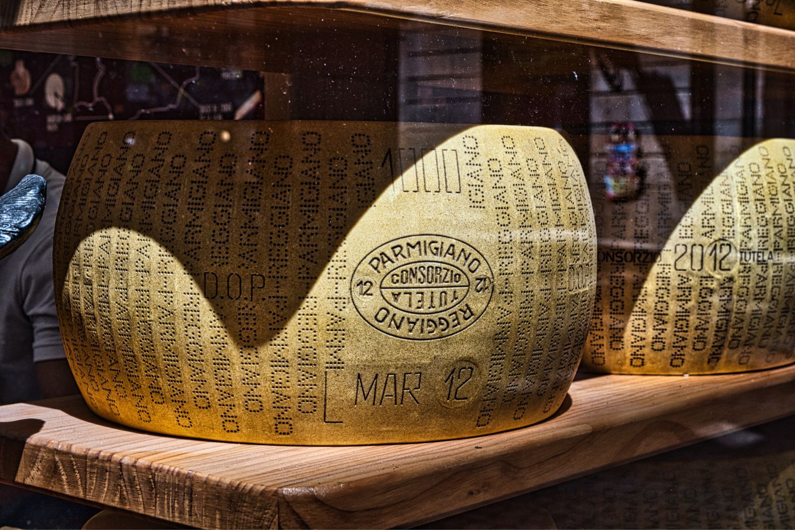 Large cheese with printed text displayed on a wooden tray in a shop window.