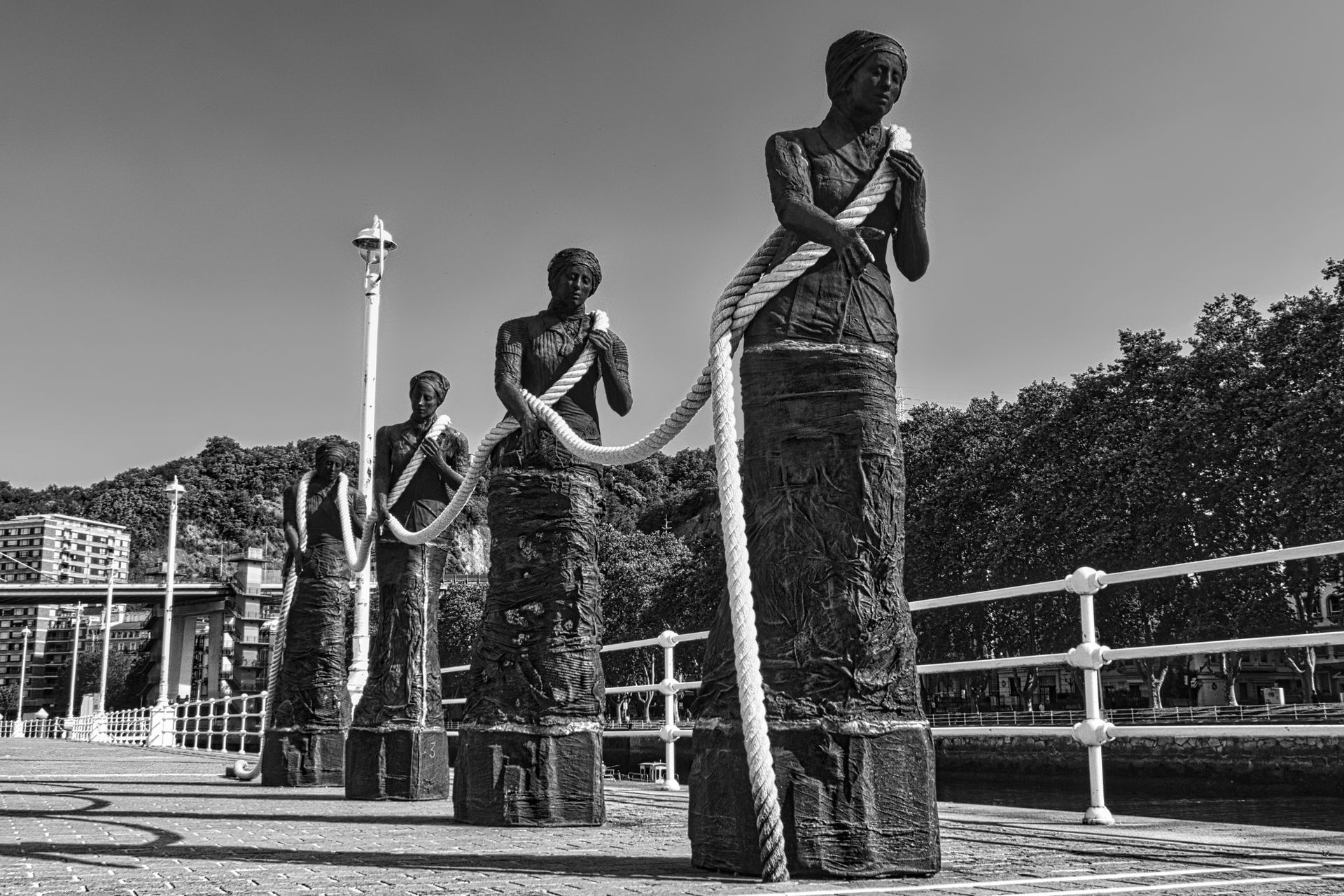 Las Sirgueras - Bilbao. Black-and-white statues of people standing in a row on a waterfront promenade