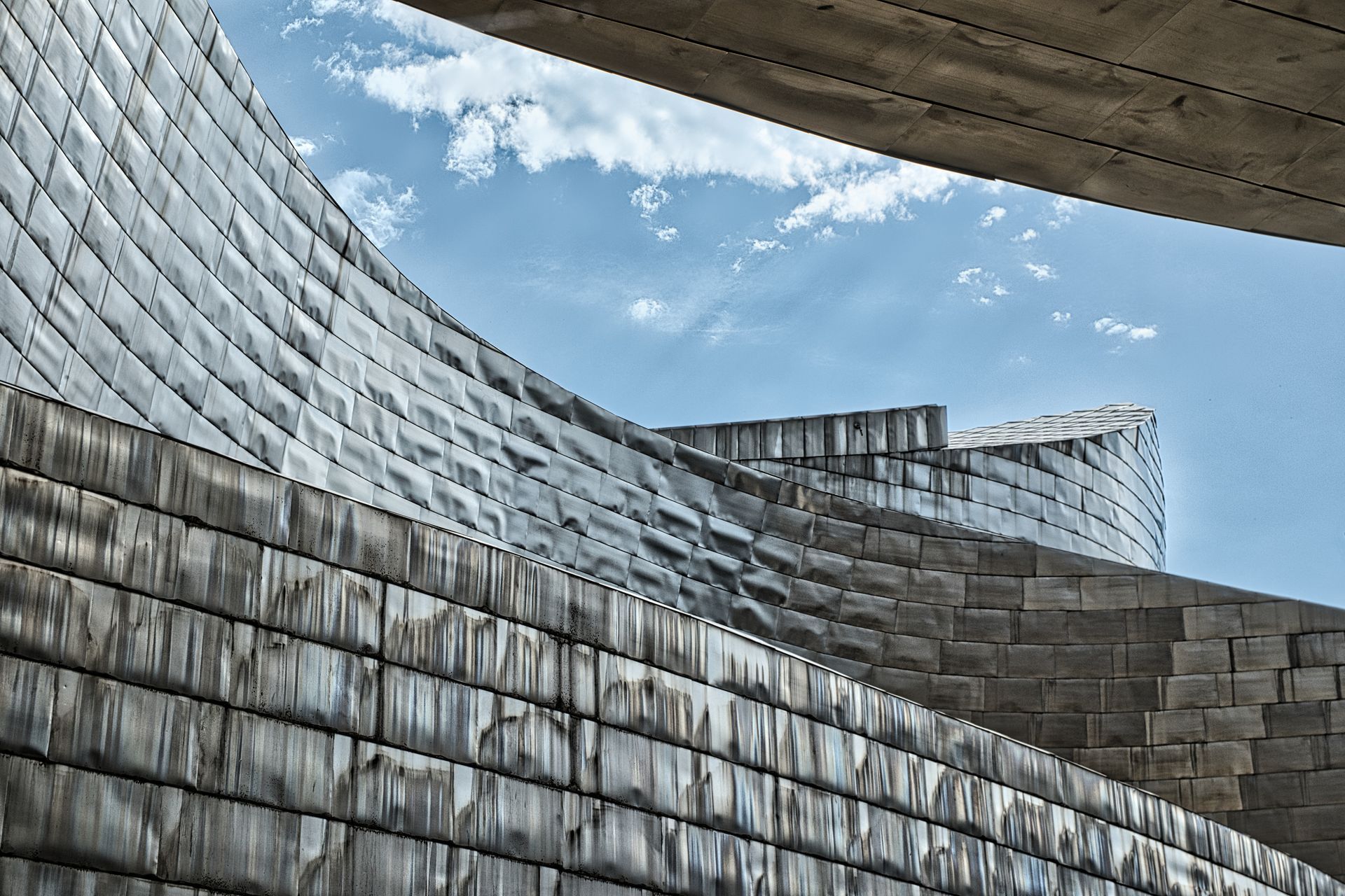Curved stone and metal architectural walls under a cloudy sky