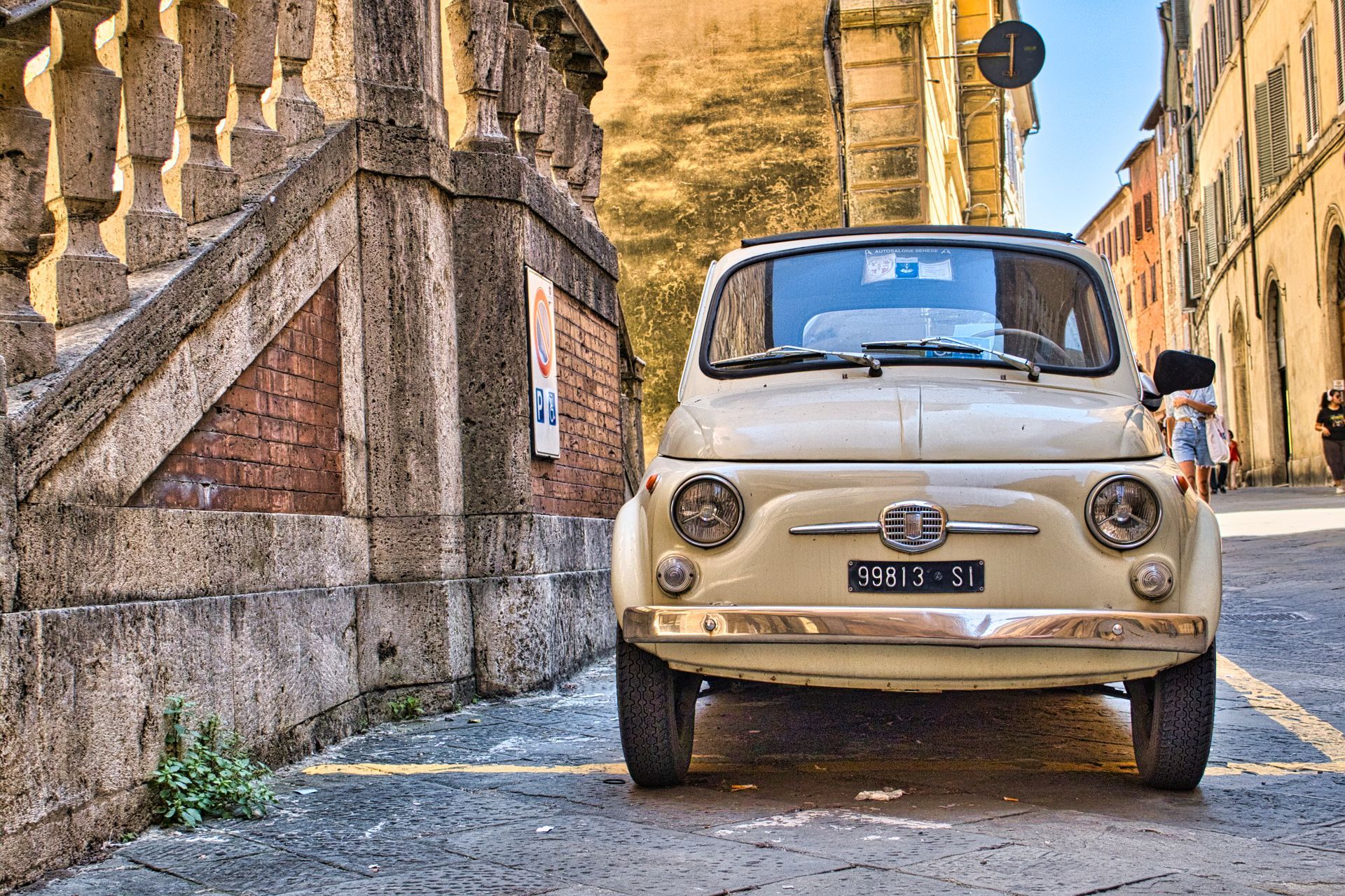 Cream vintage Fiat 500 parked on a narrow cobblestone street beside stone buildings