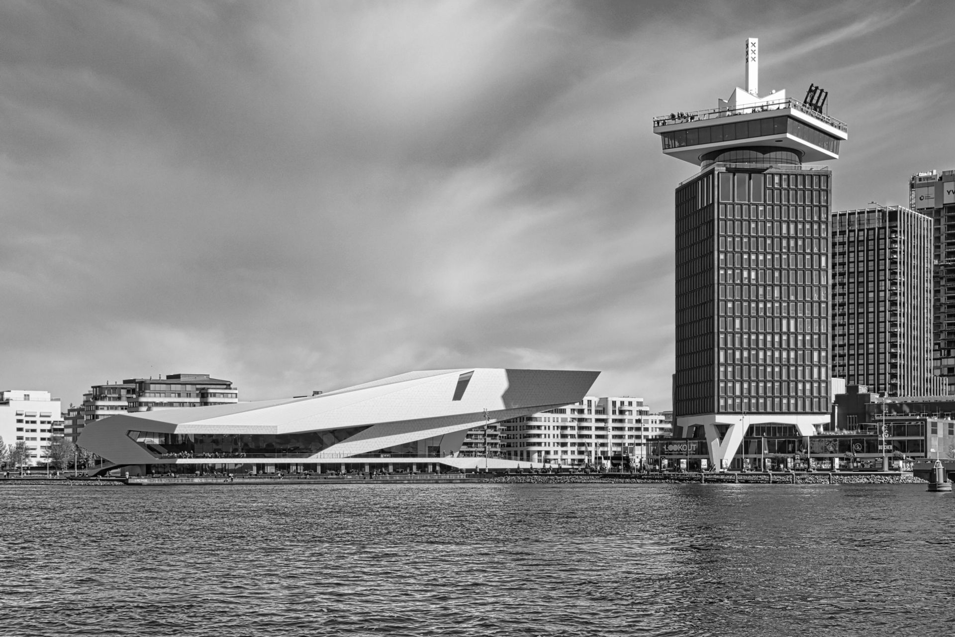 Black-and-white harbor skyline with a modern waterfront building and tall tower by the water