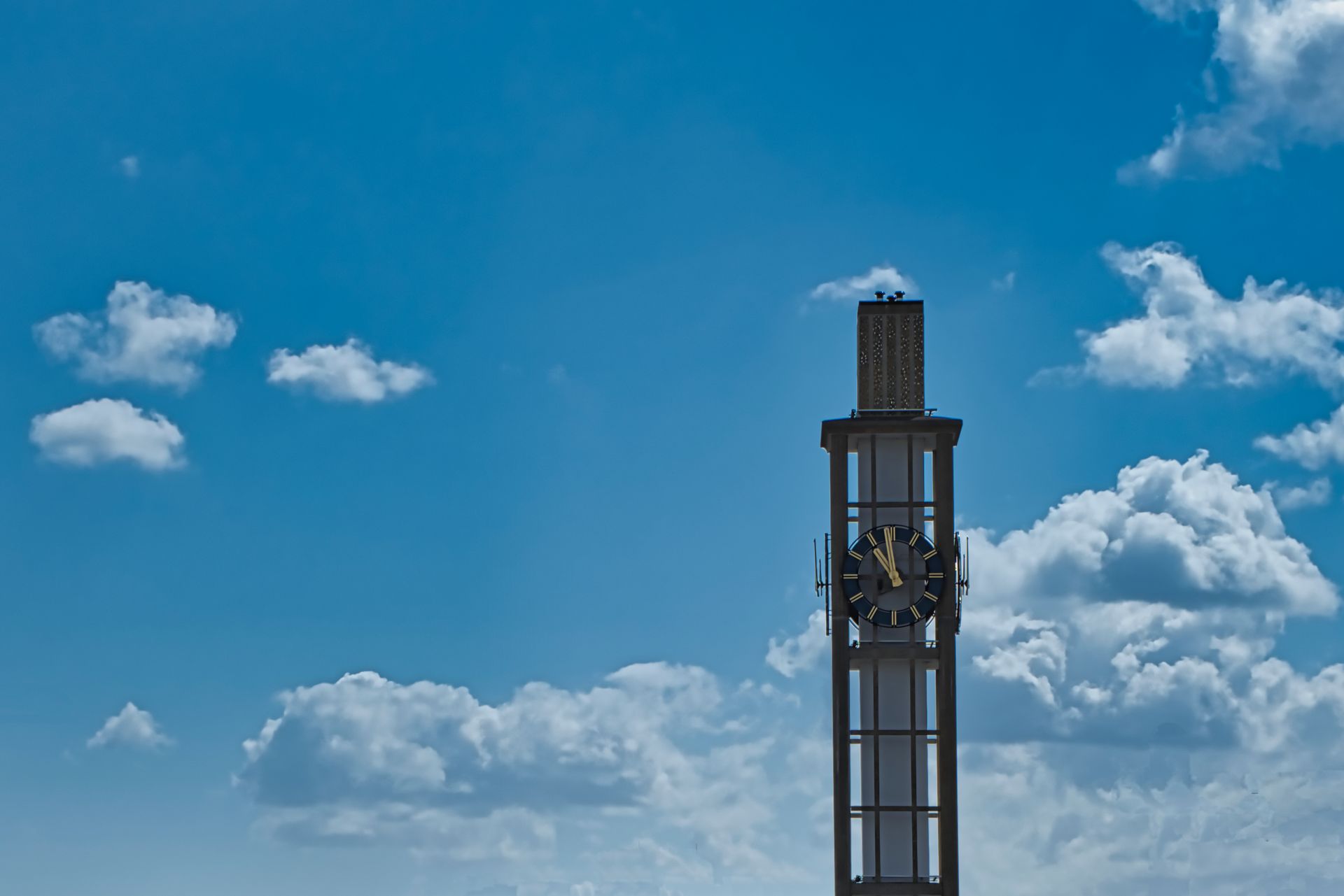 Tall industrial tower against a bright blue sky with scattered white clouds