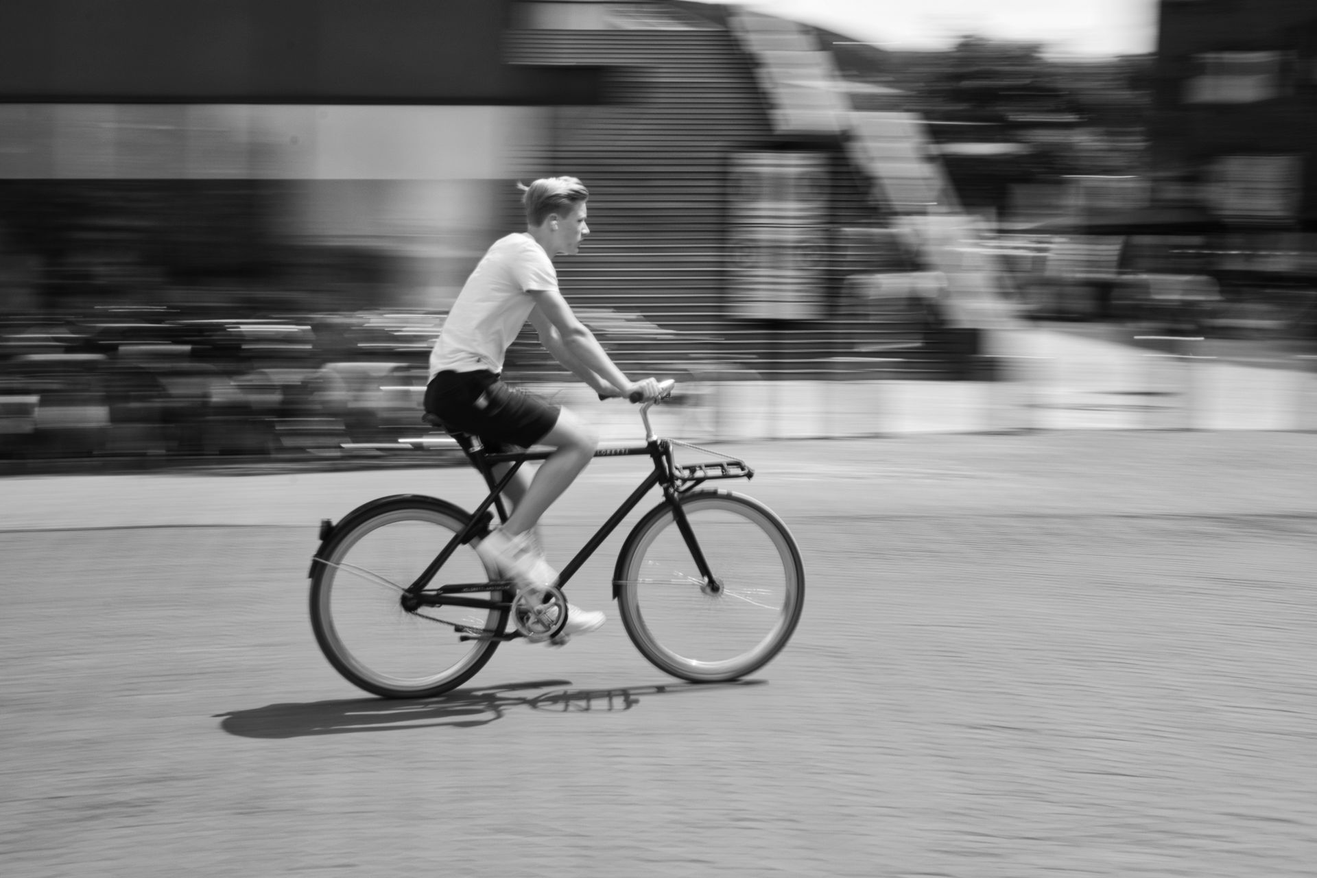 Cyclist riding a bike across a cobblestone street in a blurred black-and-white scene